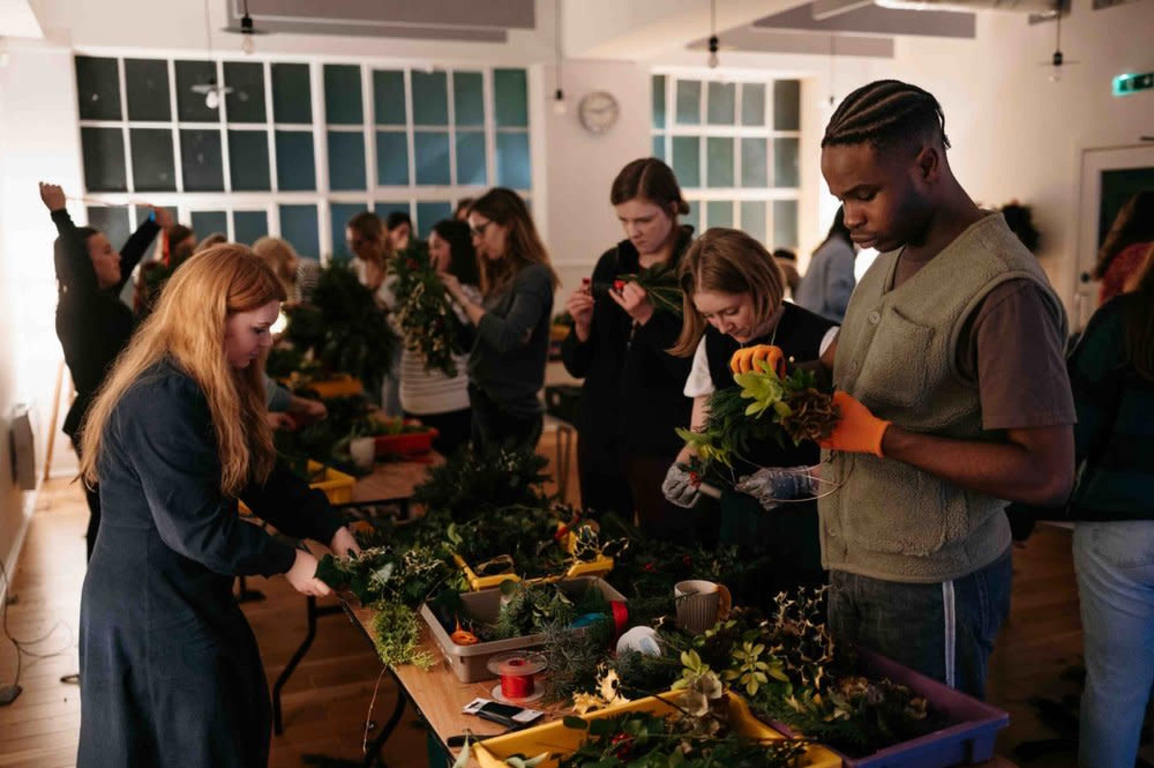 A group of people is engaged in a floral arrangement workshop, working with various plants and materials on tables.