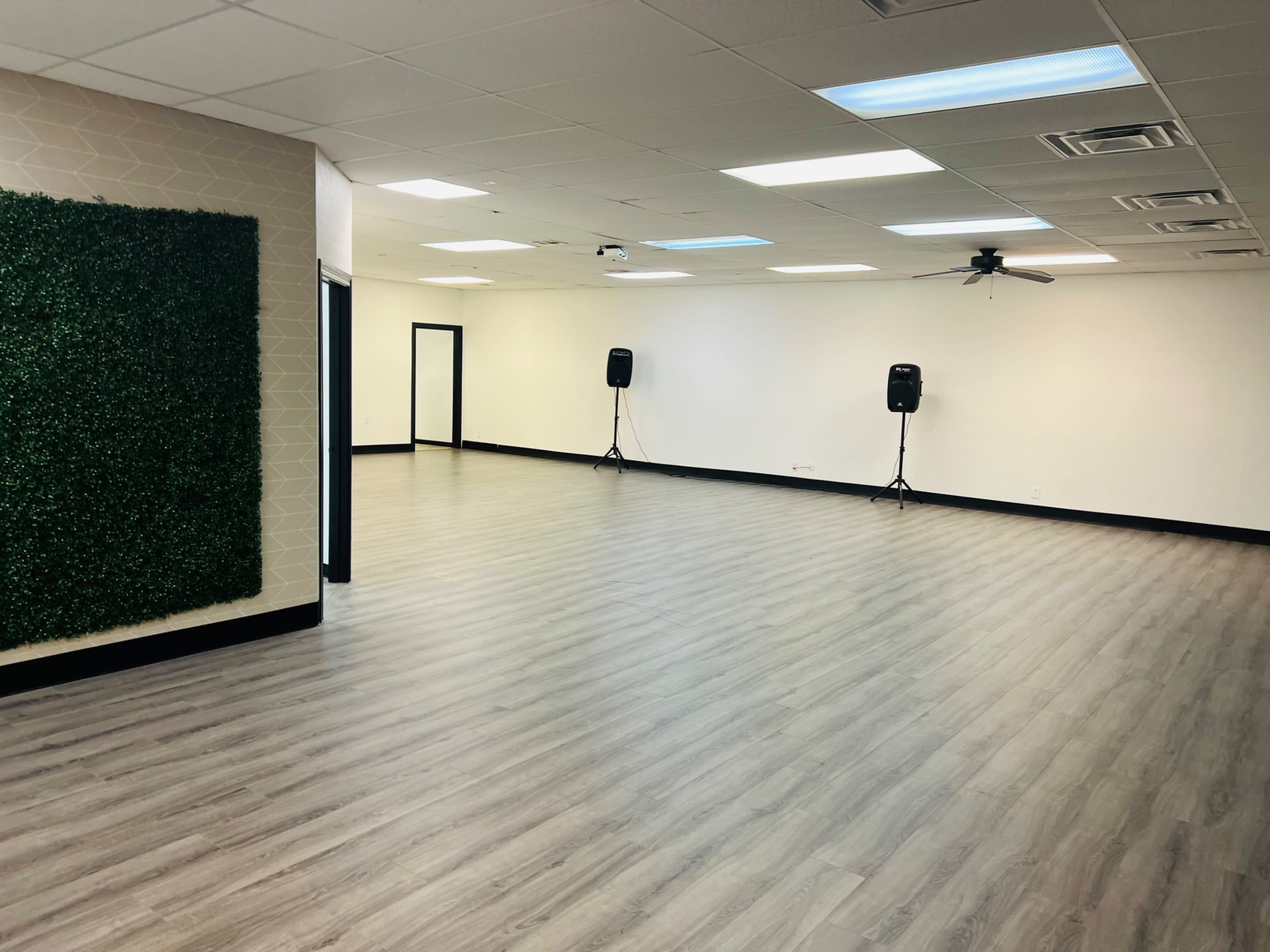 A spacious room with light wood flooring, a green accent wall, and two speakers positioned near the back walls.