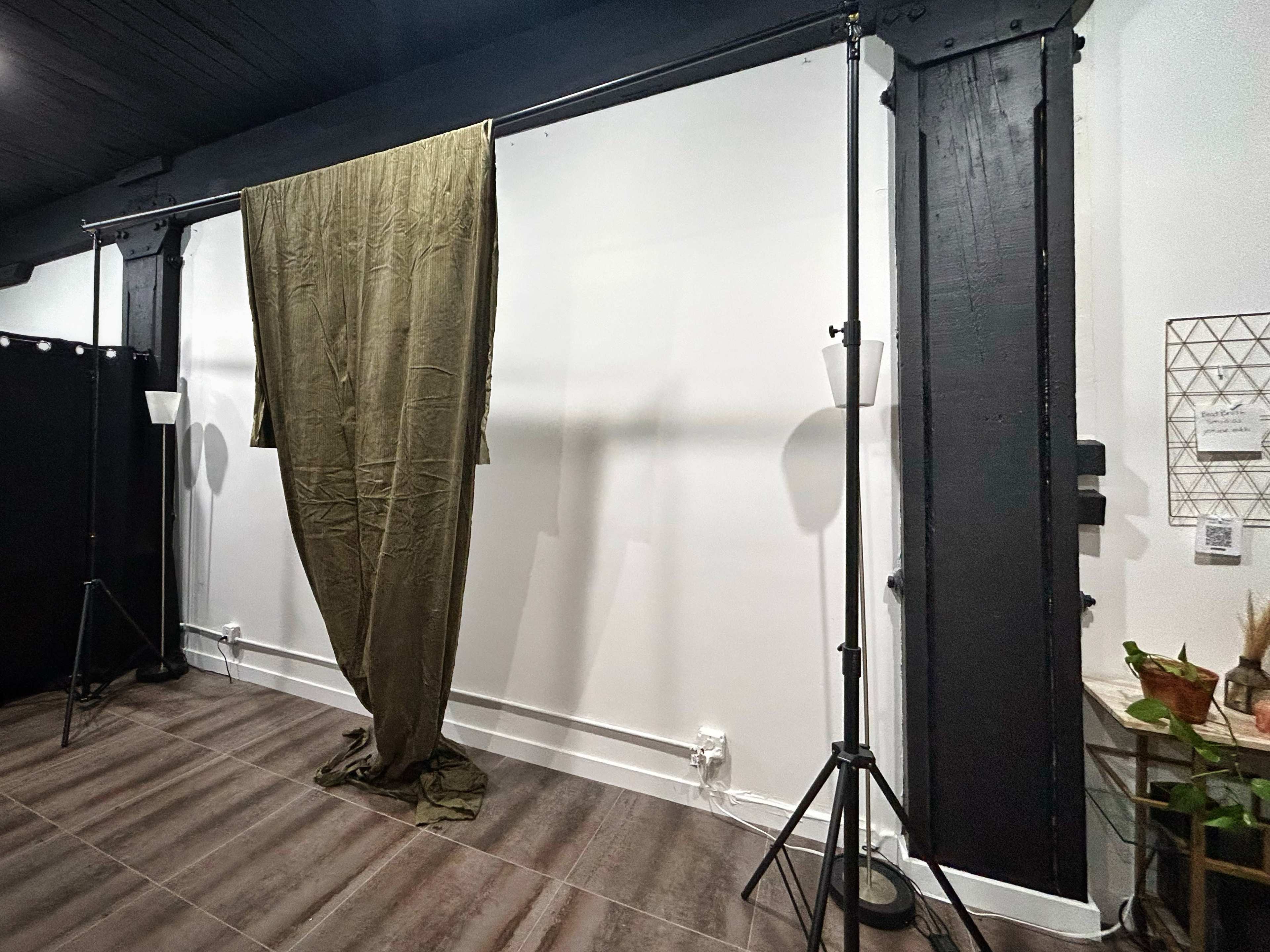 The image shows a studio space with a dark curtain hanging between two lighting stands against a blank wall.