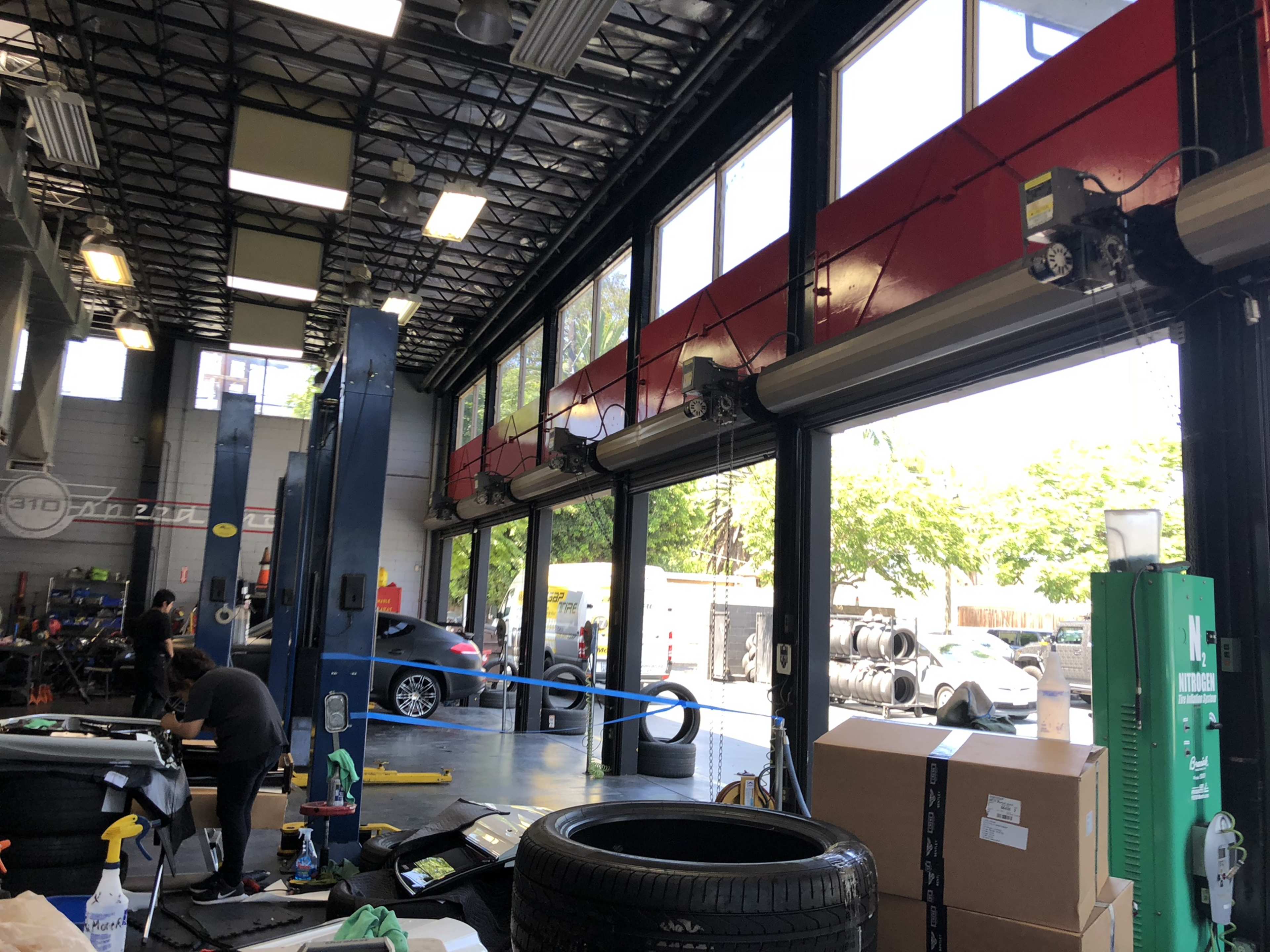 The image shows an auto repair shop with large windows, displaying tires and equipment, and workers engaged in various tasks.