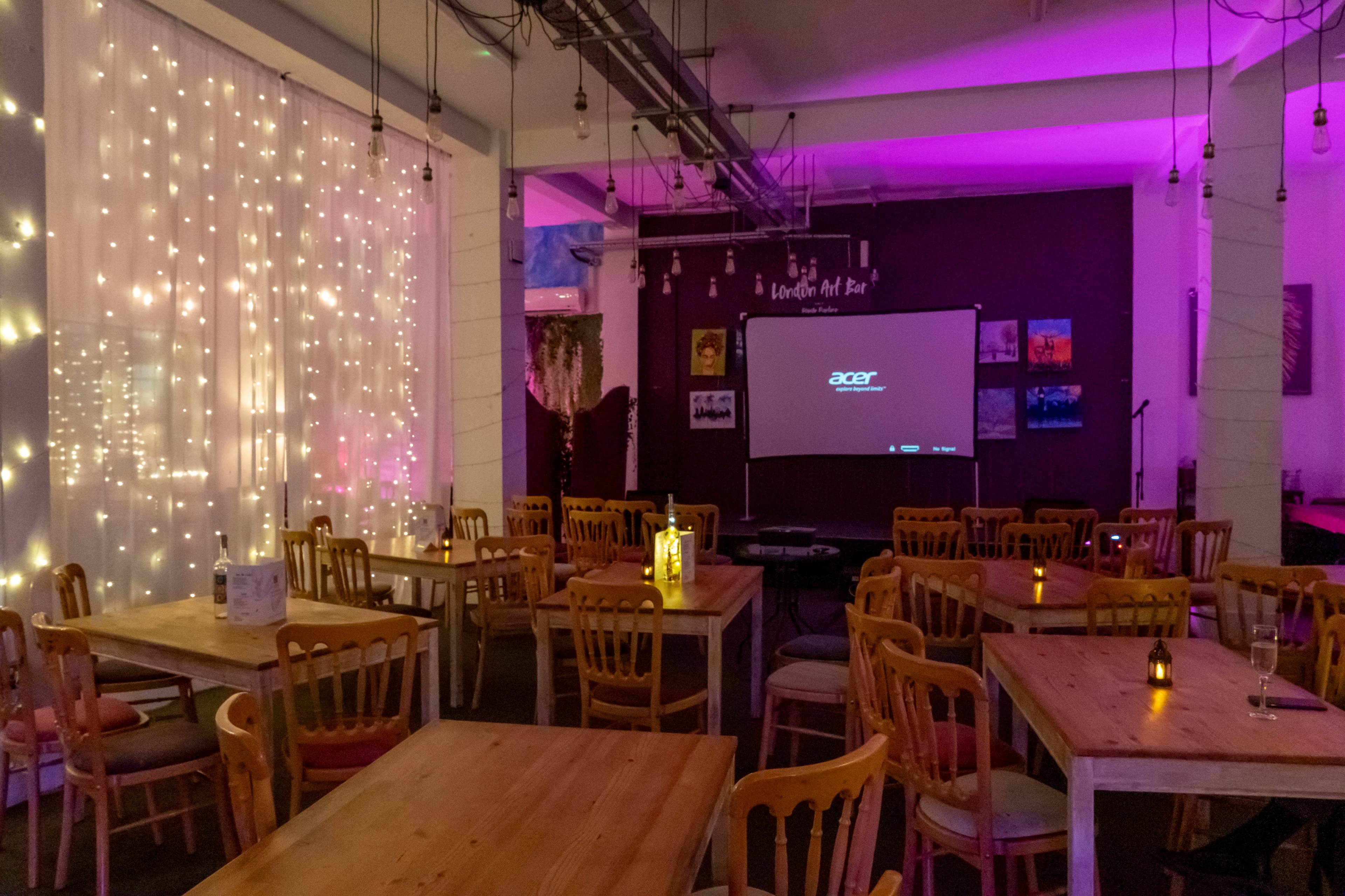 The image shows a dimly lit restaurant with wooden tables, chairs, and decorative string lights, featuring a projector screen at the front displaying the Acer logo.