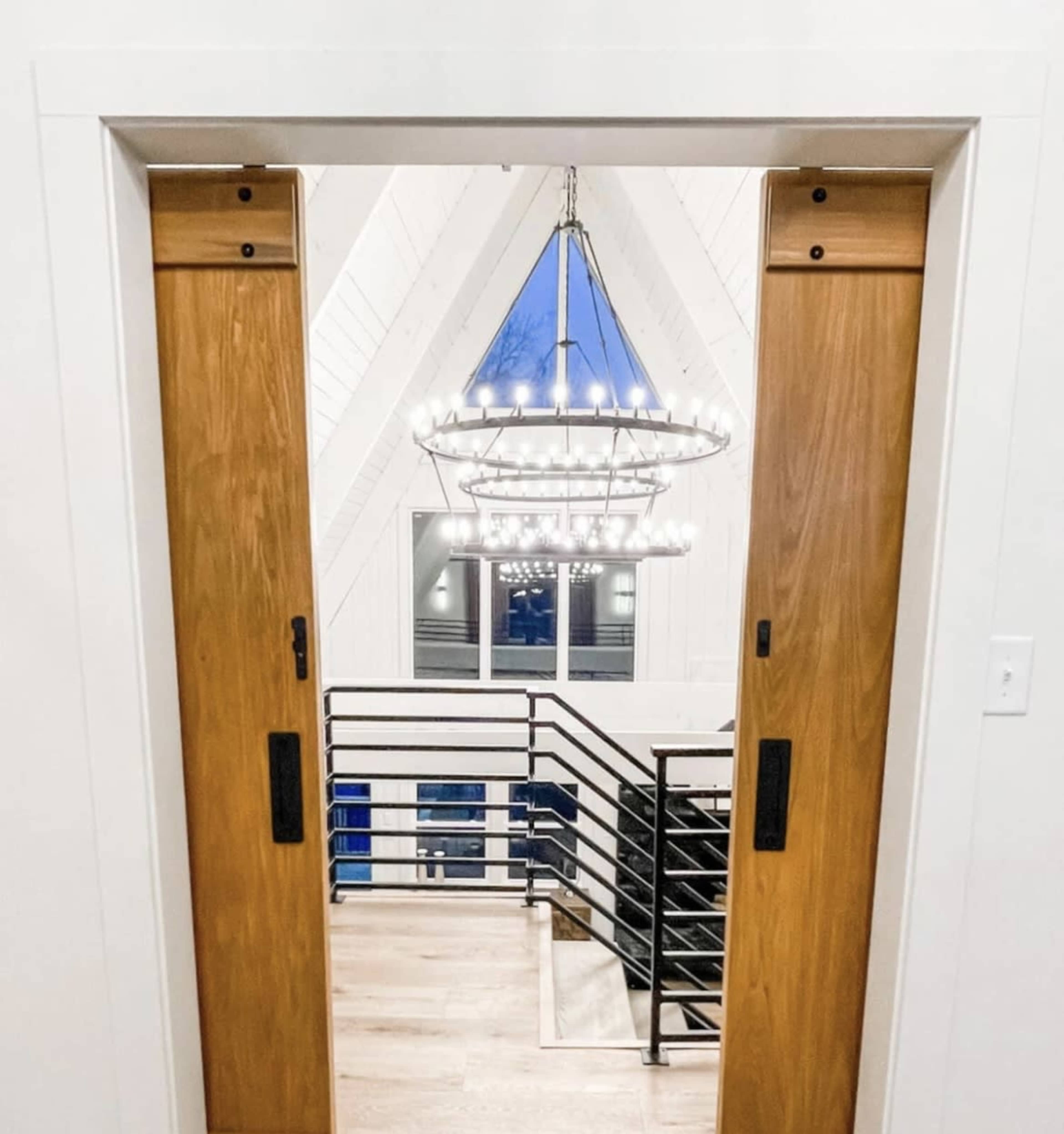 An interior view of an open doorway framed by wooden sliding doors, leading to a staircase with a modern chandelier overhead.