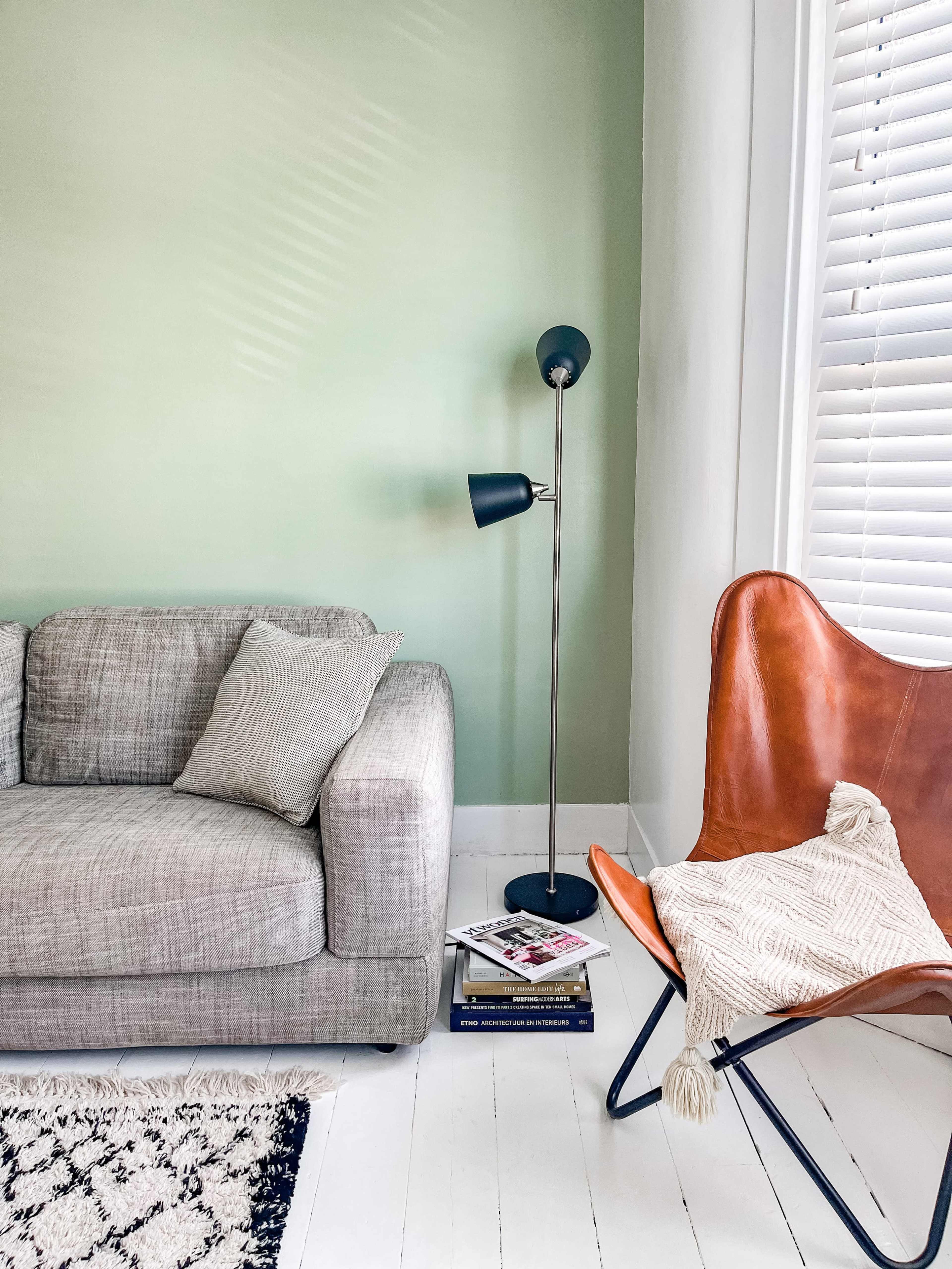 A cozy living area featuring a gray sofa, a brown leather chair, a floor lamp, and a stack of magazines on the floor.