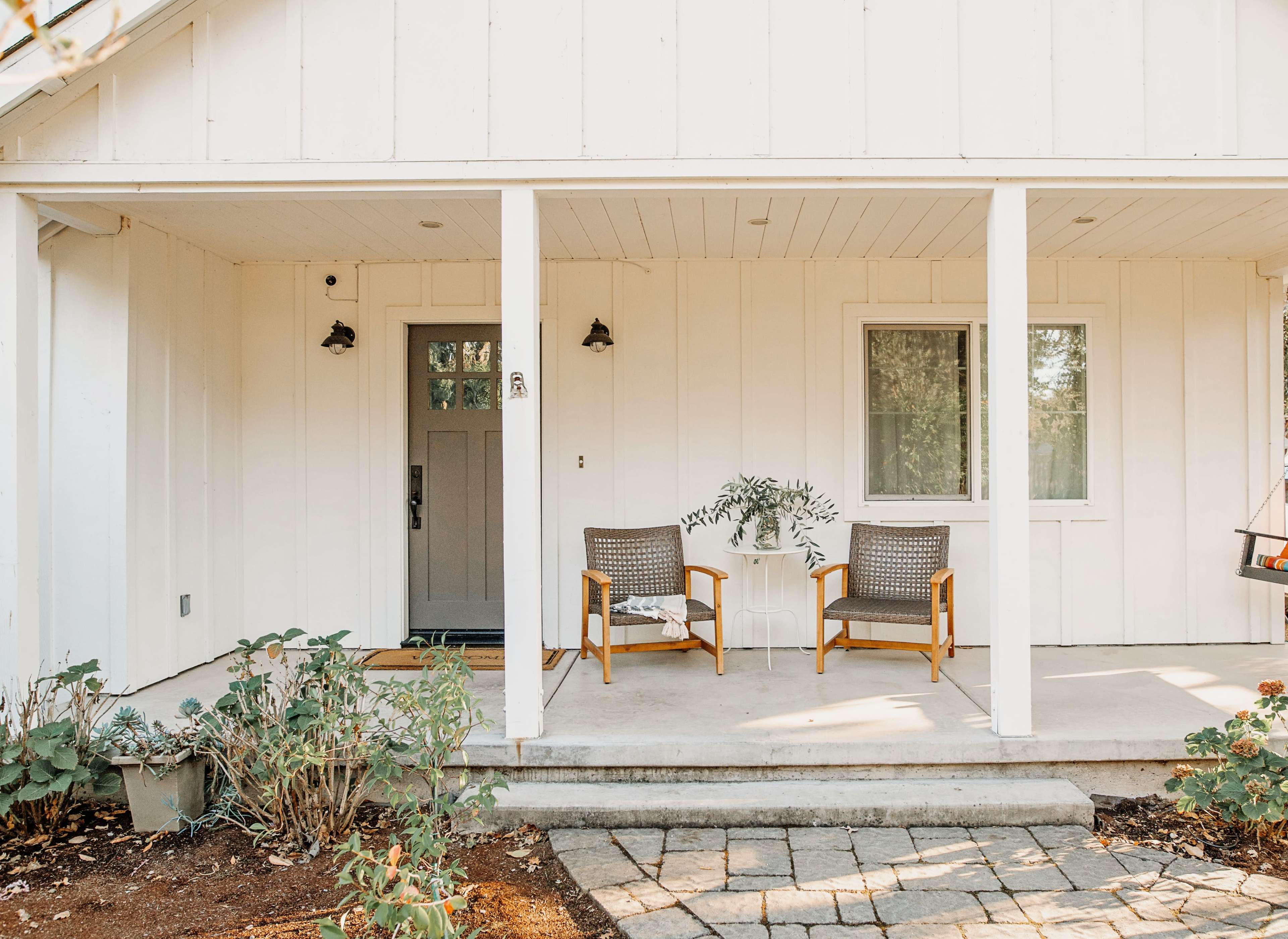 A front porch with two chairs and a small table, surrounded by plants and pavers.