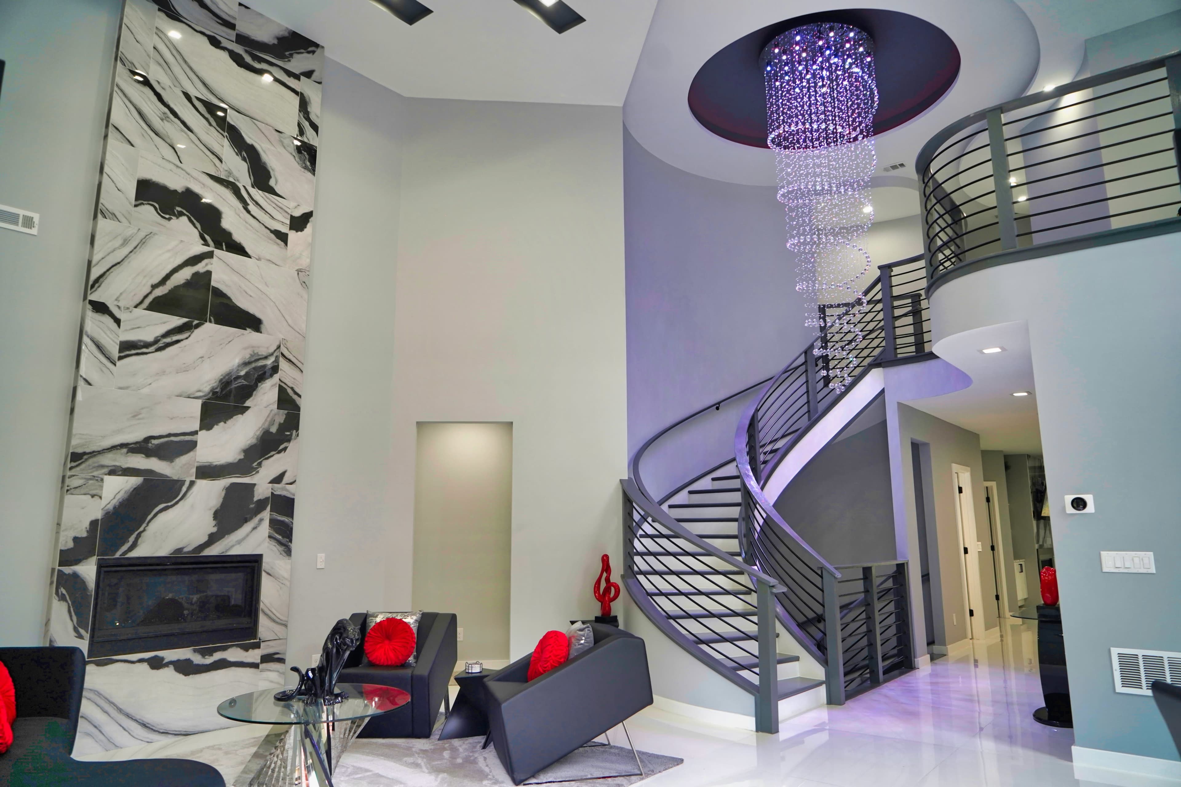 A modern living space featuring a spiral staircase, a marble accent wall, and a contemporary chandelier.
