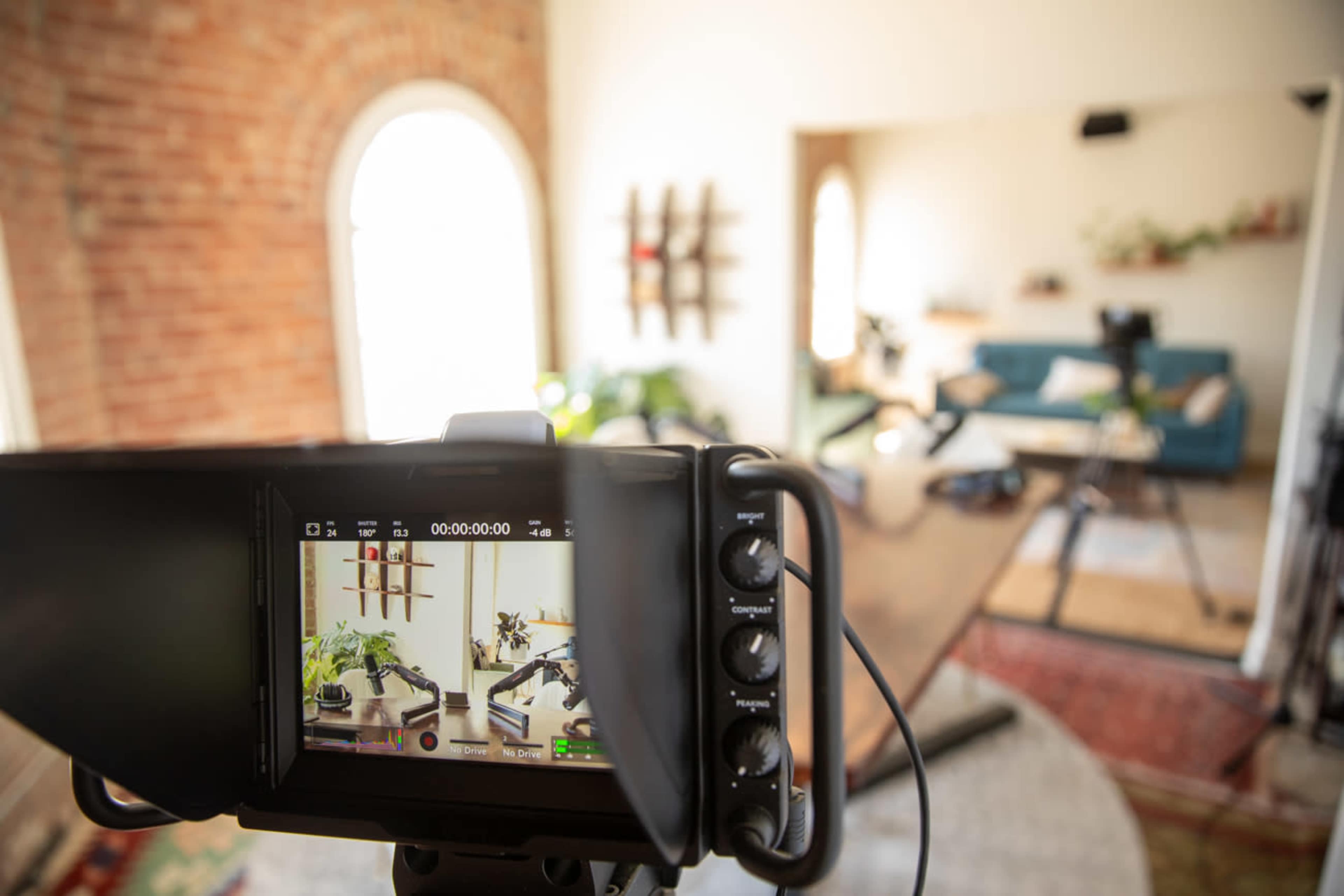 A camera is focused on a well-decorated interior space with plants, a large table, and a blue sofa.