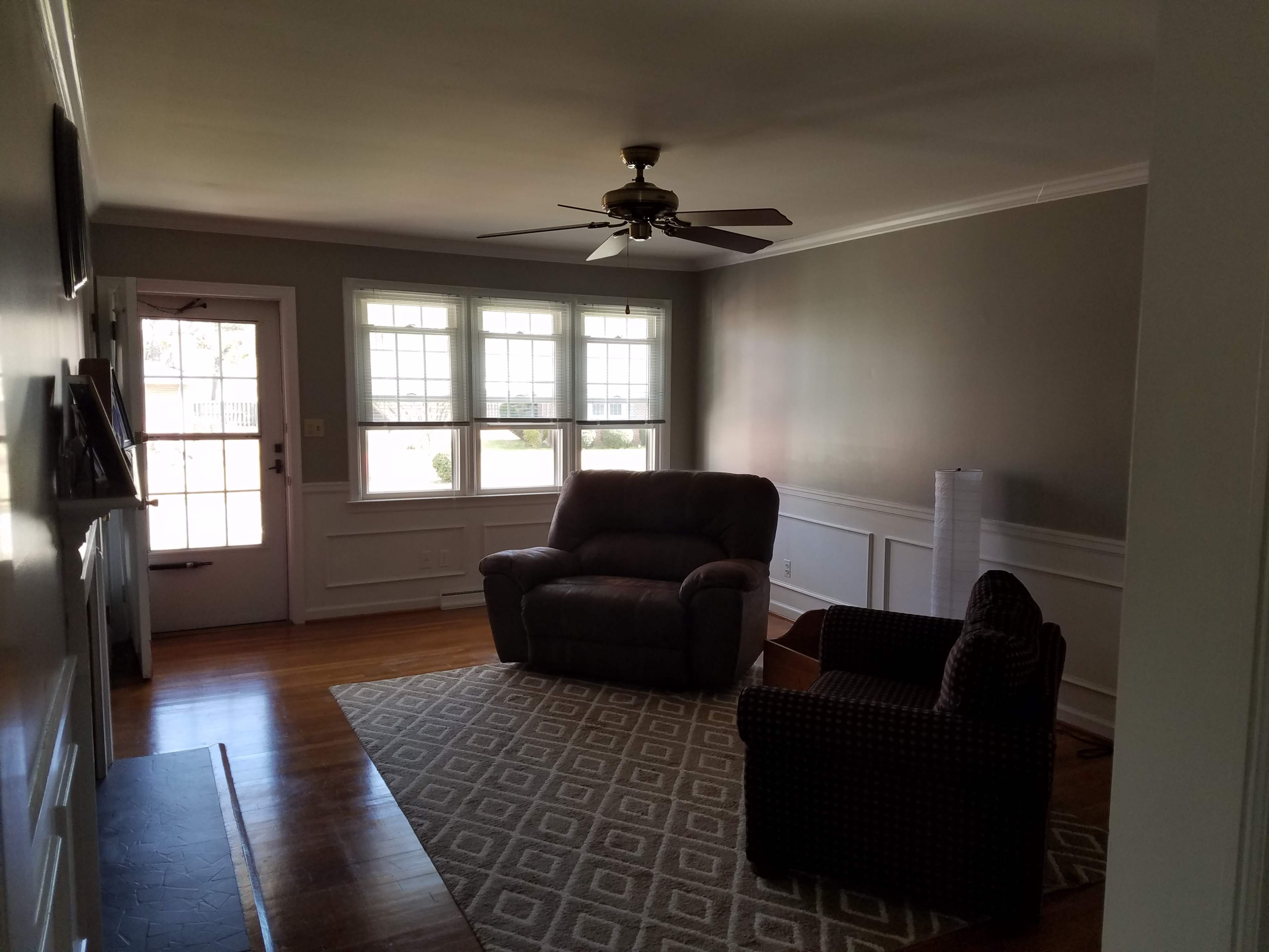 A living room with two chairs, a ceiling fan, and large windows letting in natural light.