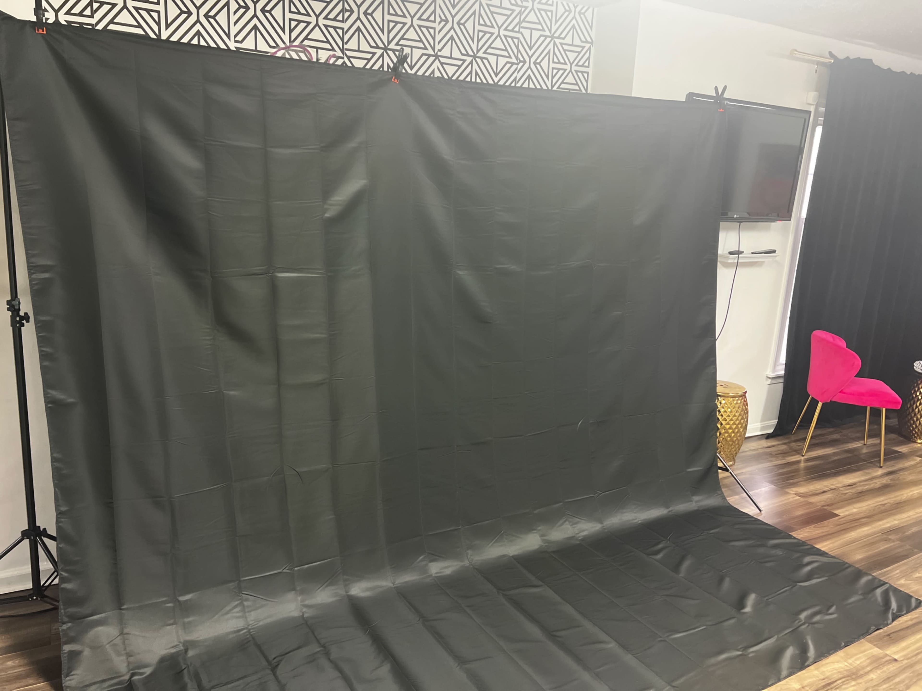 A large, dark fabric backdrop set up in a room with wooden flooring and a few visible studio lights.