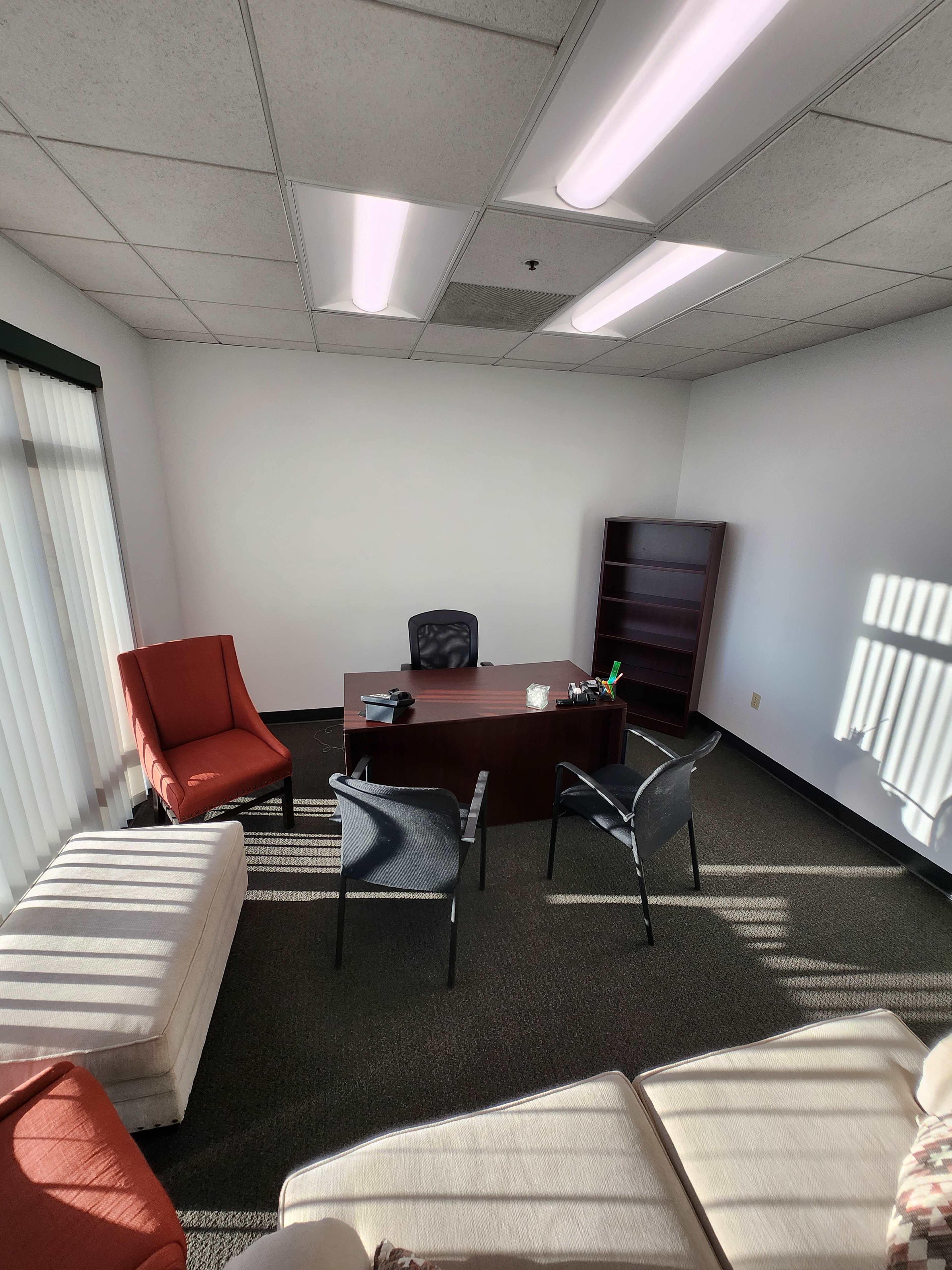 The image shows an office space with a desk, chairs, and a bookshelf, illuminated by overhead lighting.