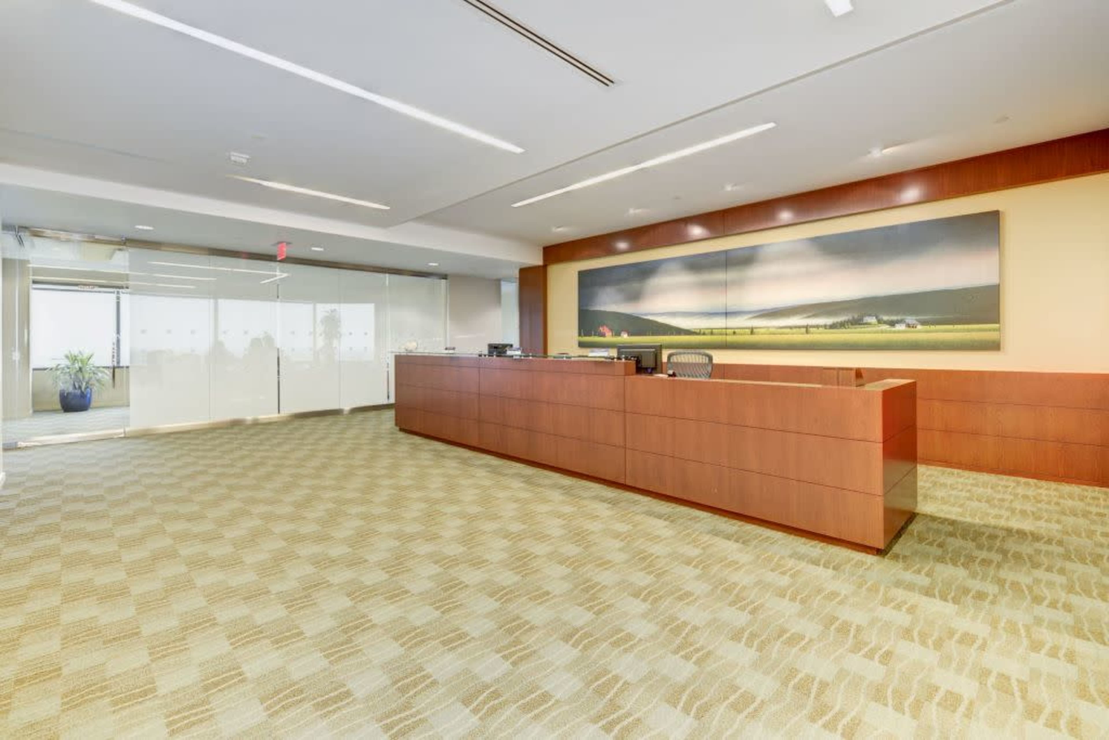 The image shows a clean and modern office reception area with a wooden front desk and a large artwork on the wall.