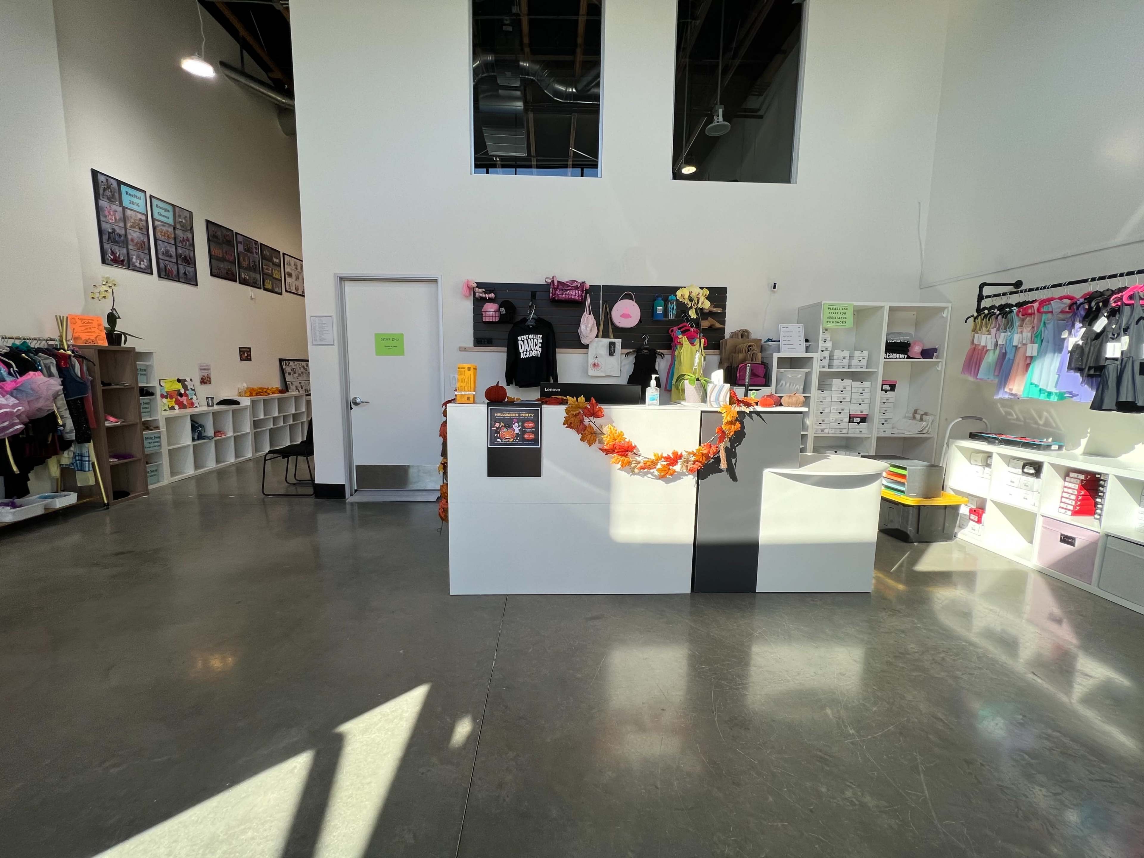 A brightly lit retail space with a reception desk adorned with decorations, shelves displaying various items, and wall-mounted photographs.