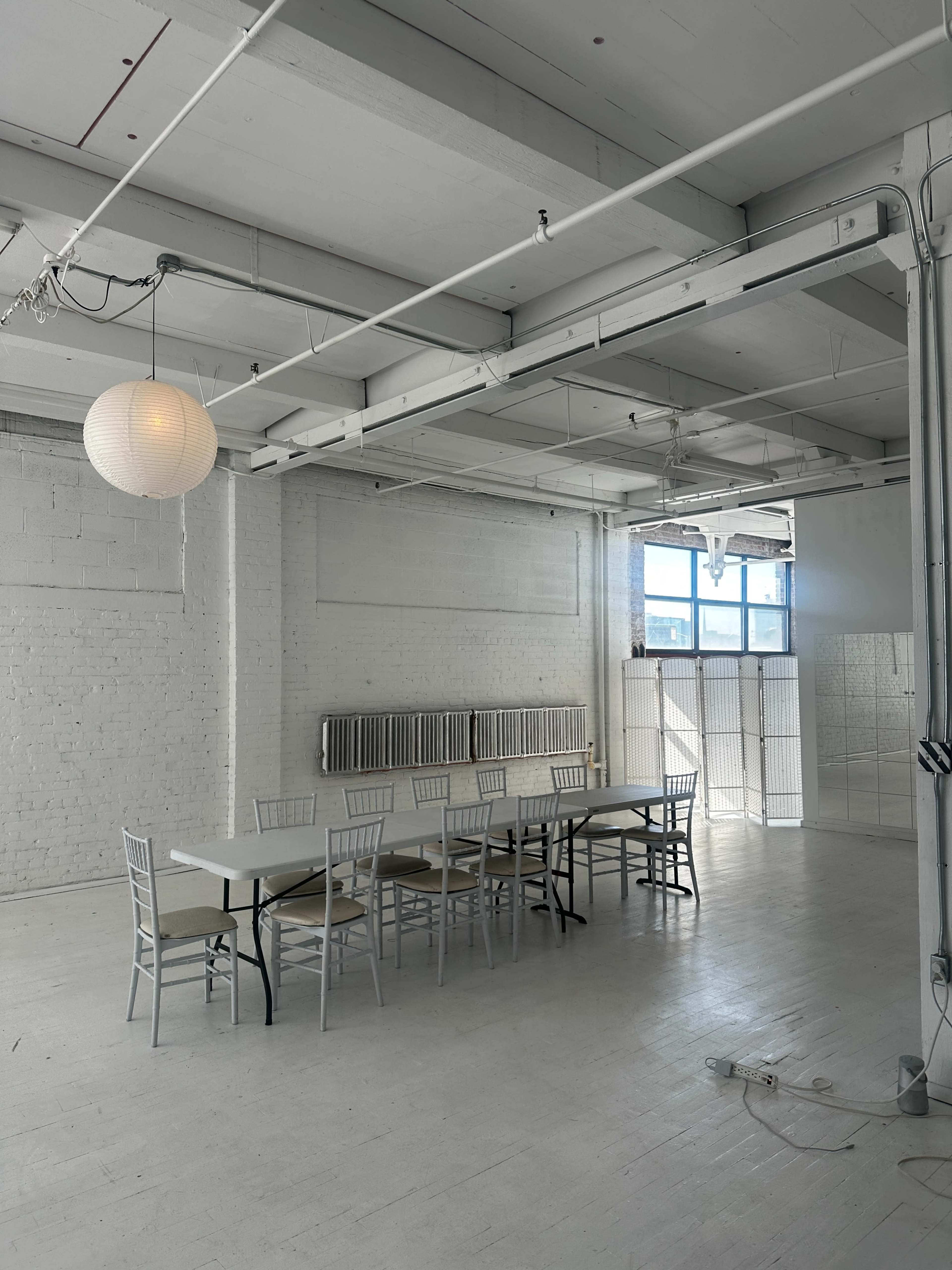 A spacious room with a long table and chairs, illuminated by a lantern, features white walls and large windows.