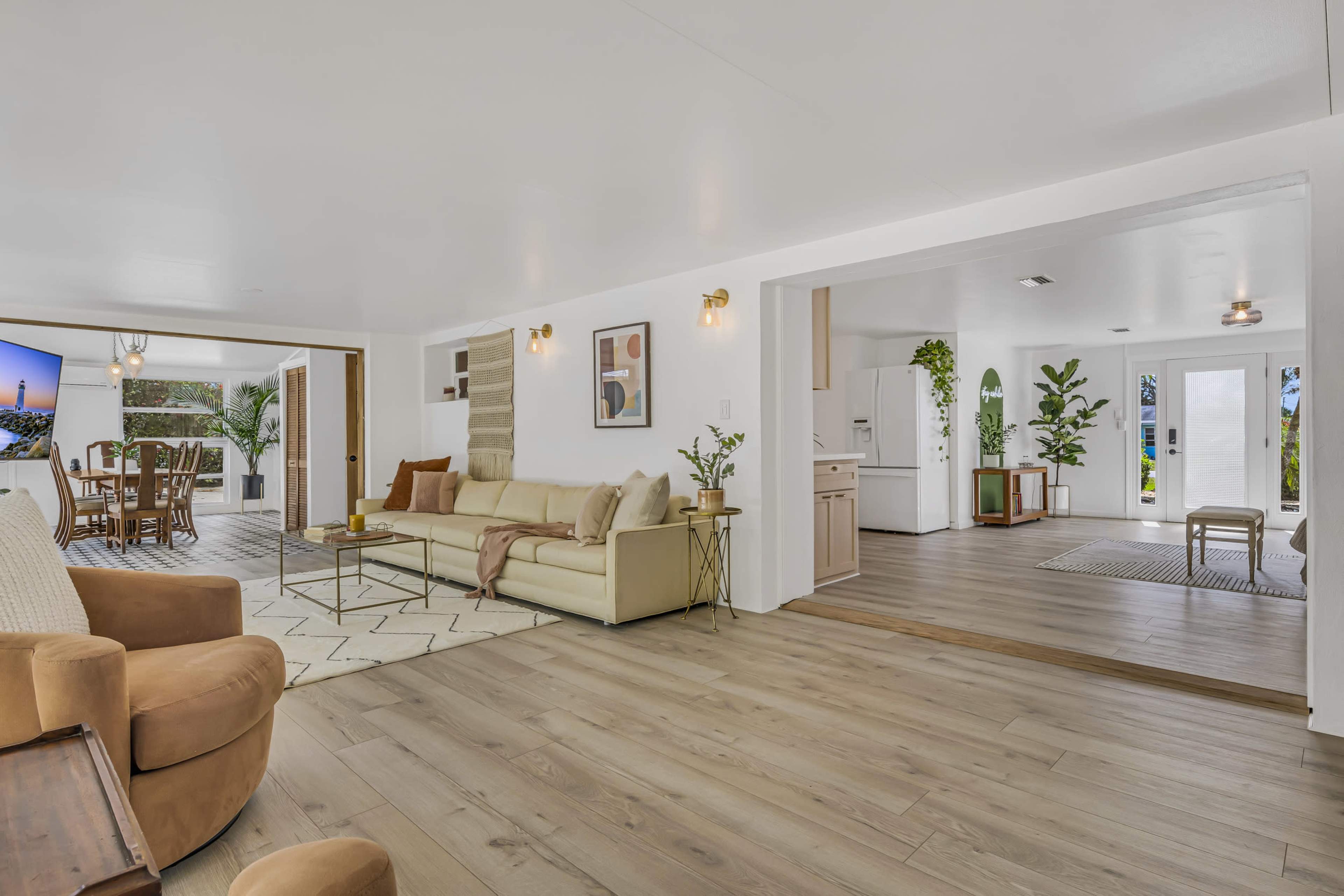 A modern, open-concept living space featuring a beige sofa, a dining area, and a kitchen, all with large windows allowing natural light.