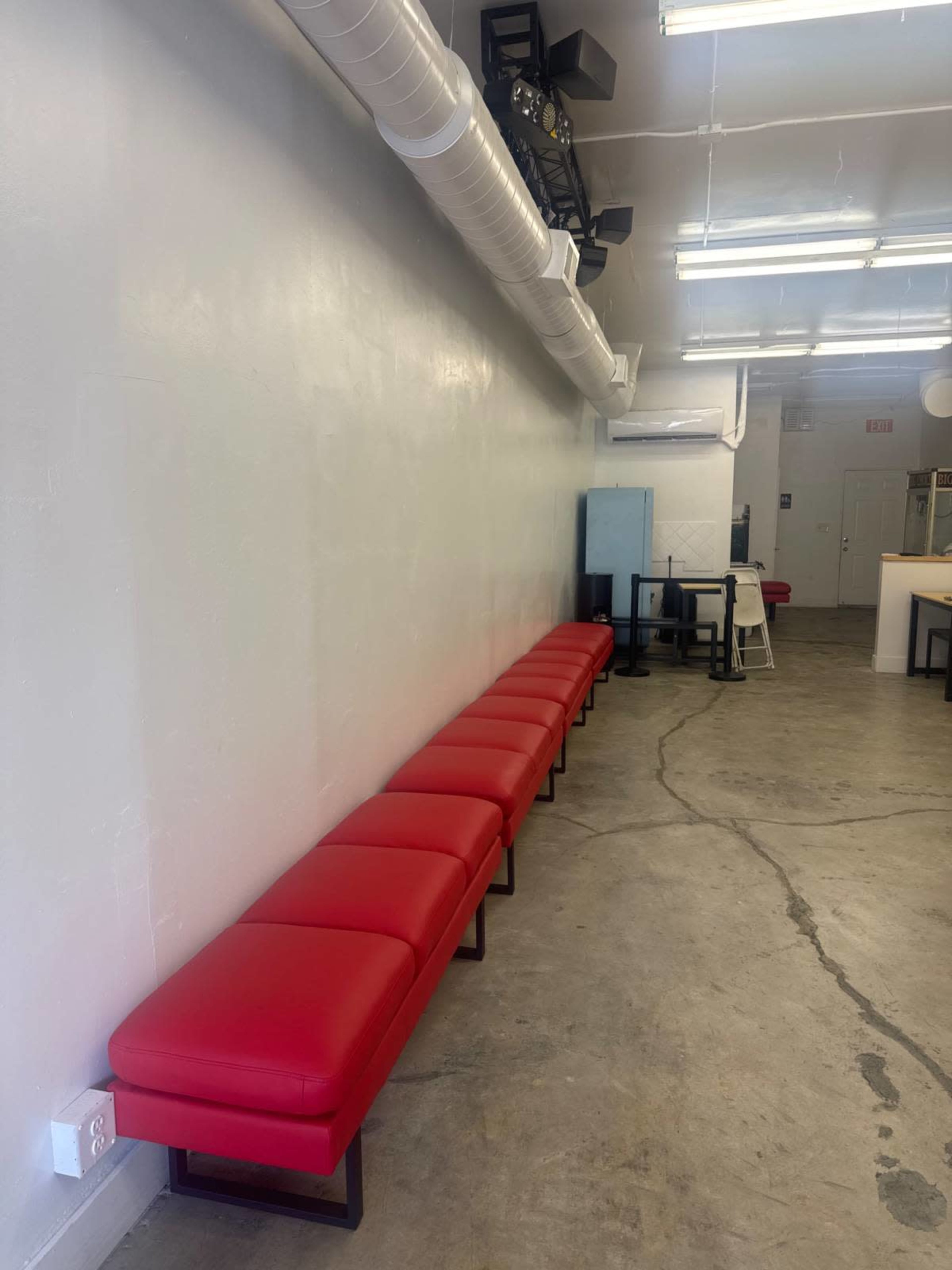 The image shows a row of red benches against a plain white wall in a spacious interior.