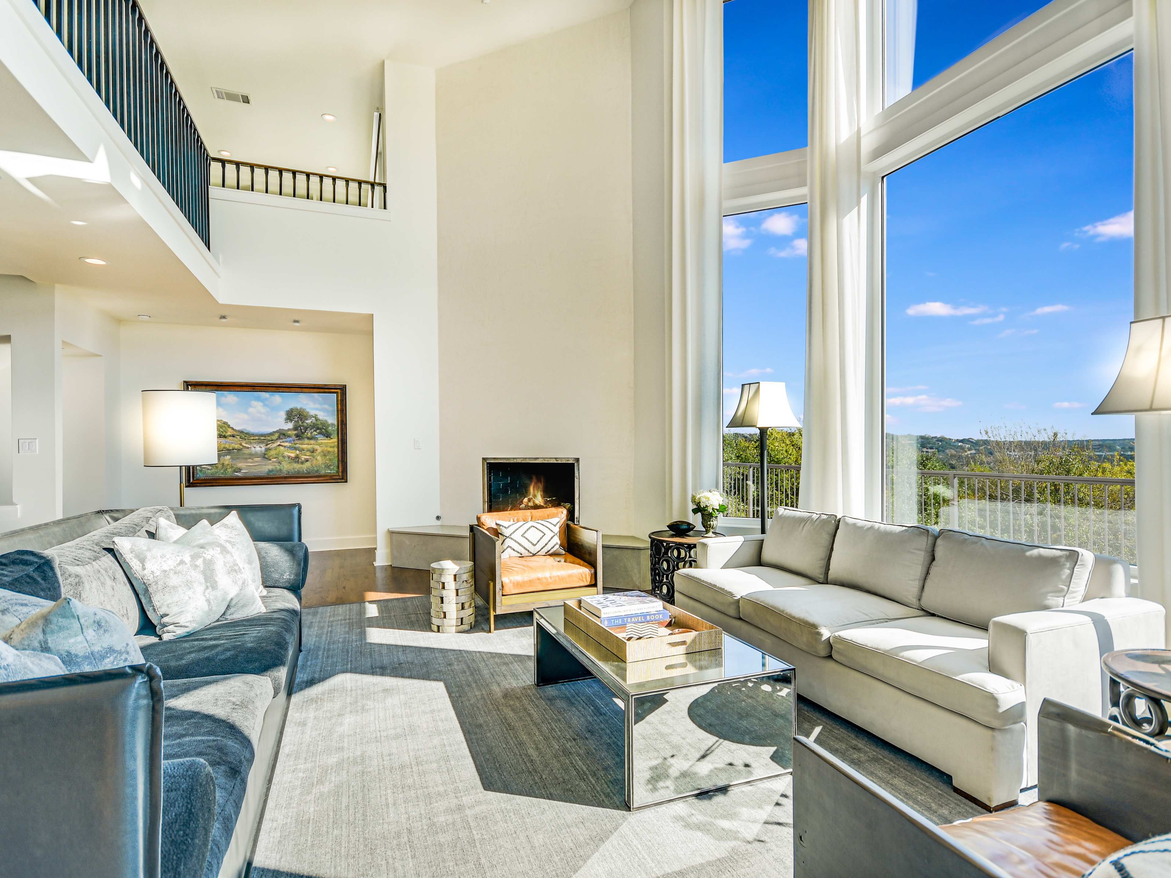 A spacious living room features large windows, a fireplace, a comfortable sofa, and a view of the outdoors.