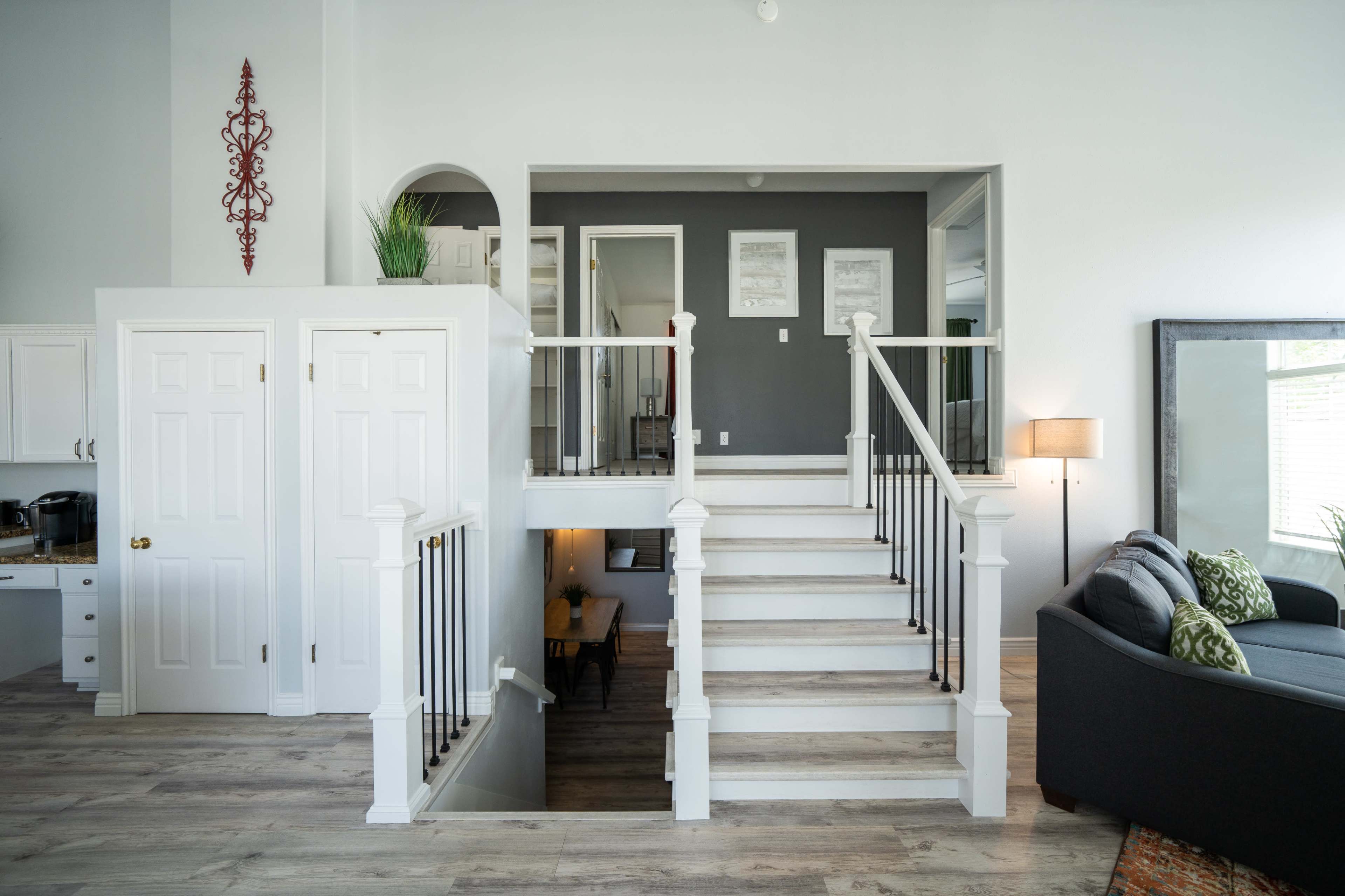 A spacious interior features white walls, a staircase with a wooden railing leading to an upper level, and a living area with a gray couch and decorative elements.