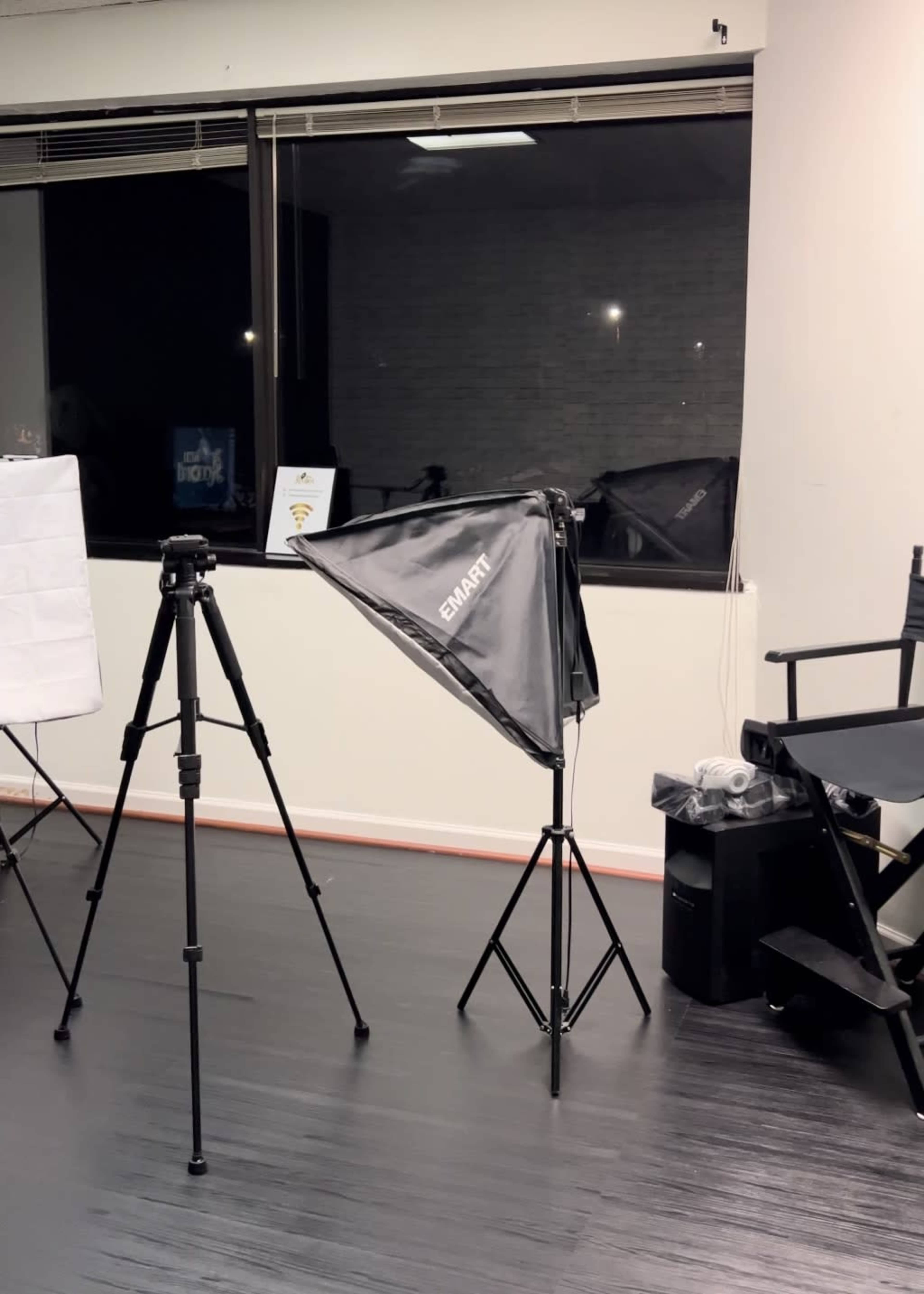 A photography setup with a tripod, a softbox light, and a director's chair in a studio environment.