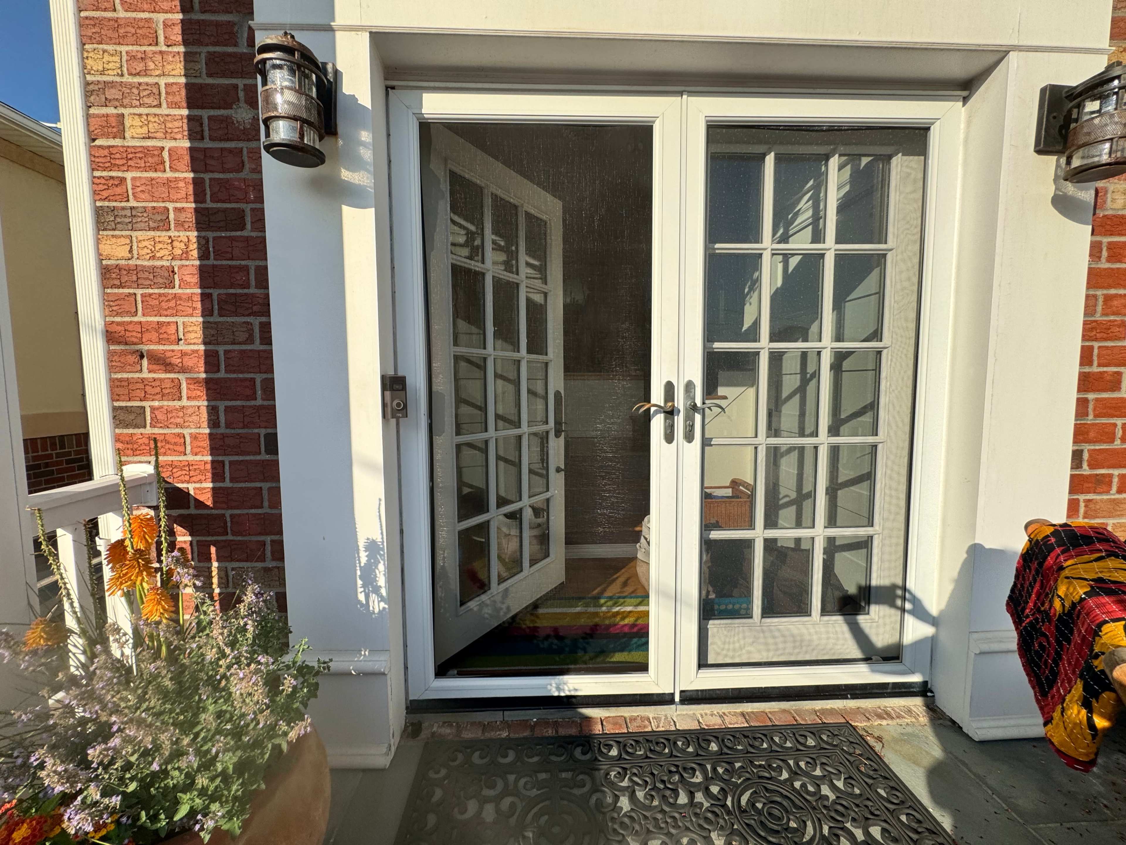 A double glass door with a screen separates the outdoor porch from the interior, surrounded by brick walls and a flower pot.