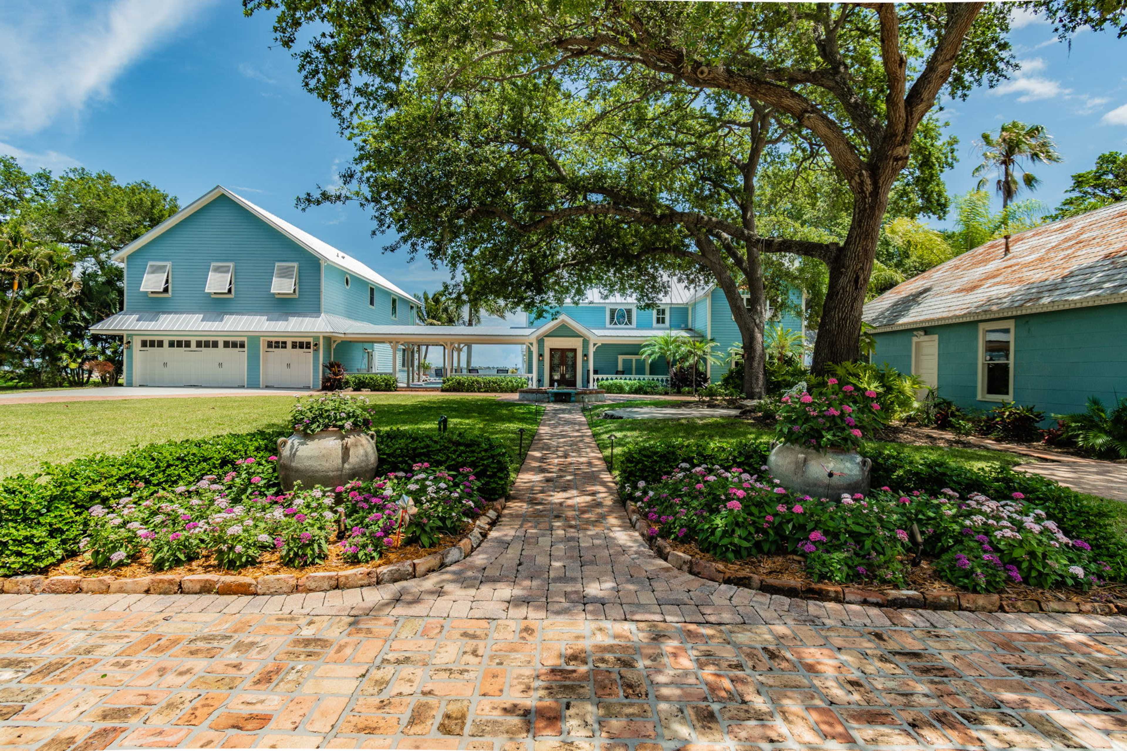 A large, light blue house surrounded by landscaped gardens with a brick pathway leading to the entrance.