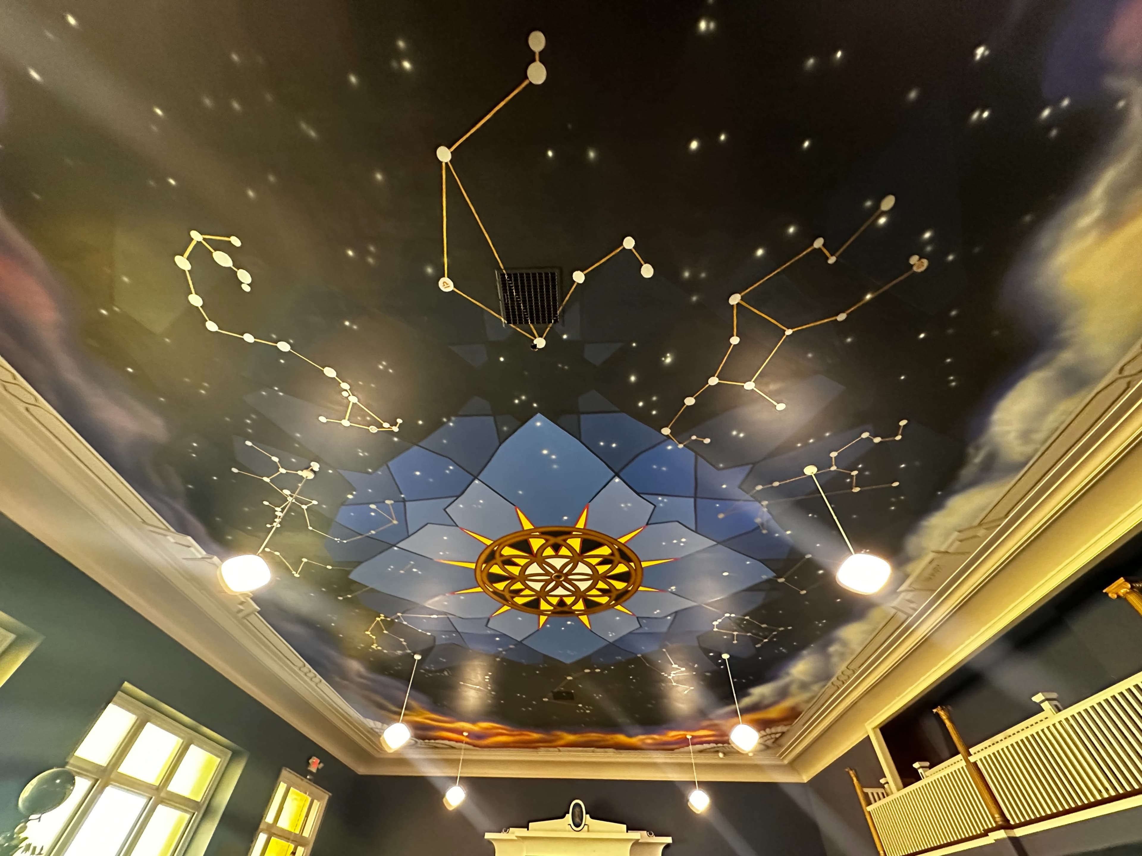 A painted ceiling featuring constellations, a central star pattern, and decorative elements in a dimly lit room.
