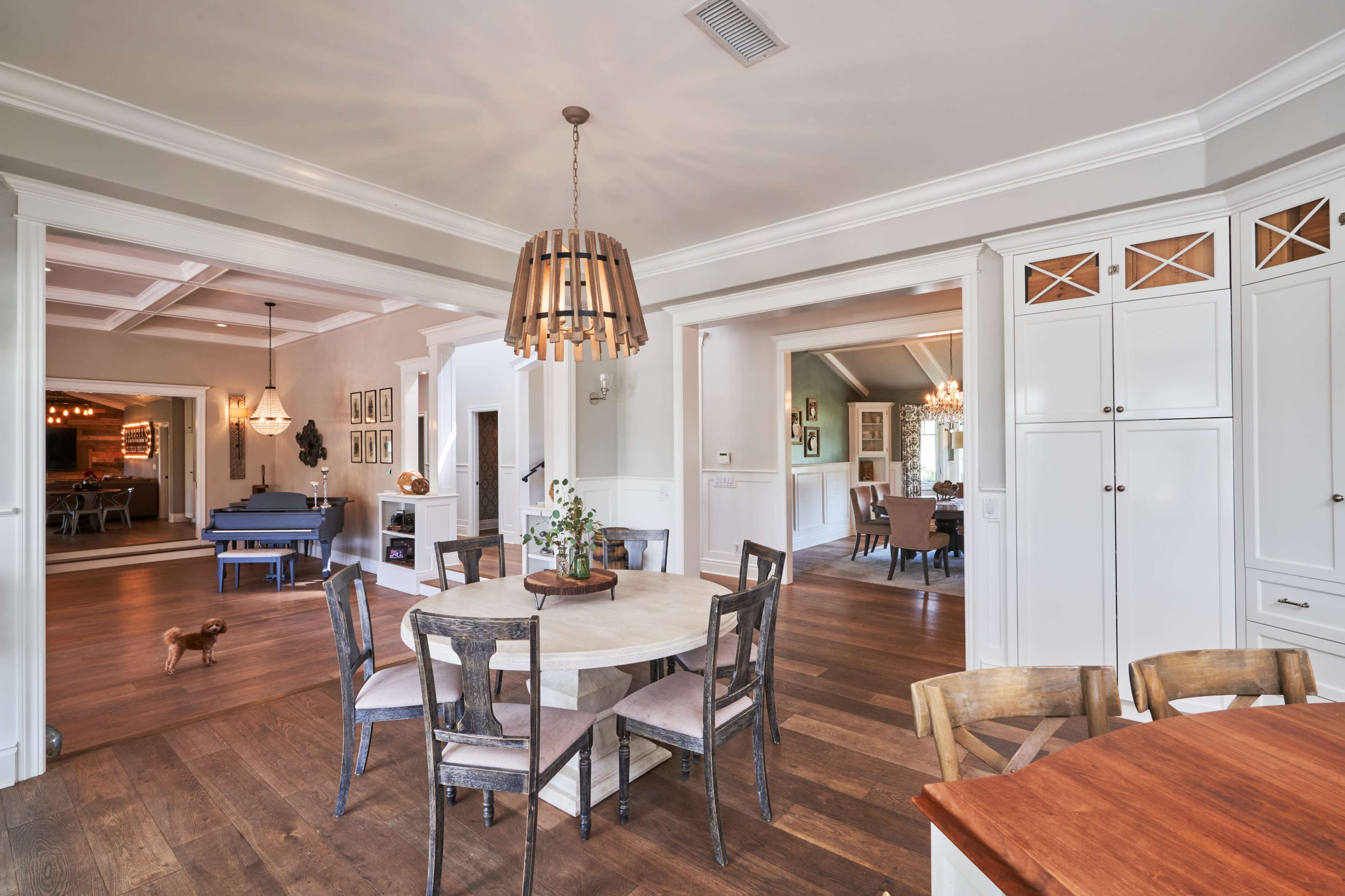 A spacious dining area with a round table surrounded by chairs, leading to an adjoining room with additional seating and a blue piano.