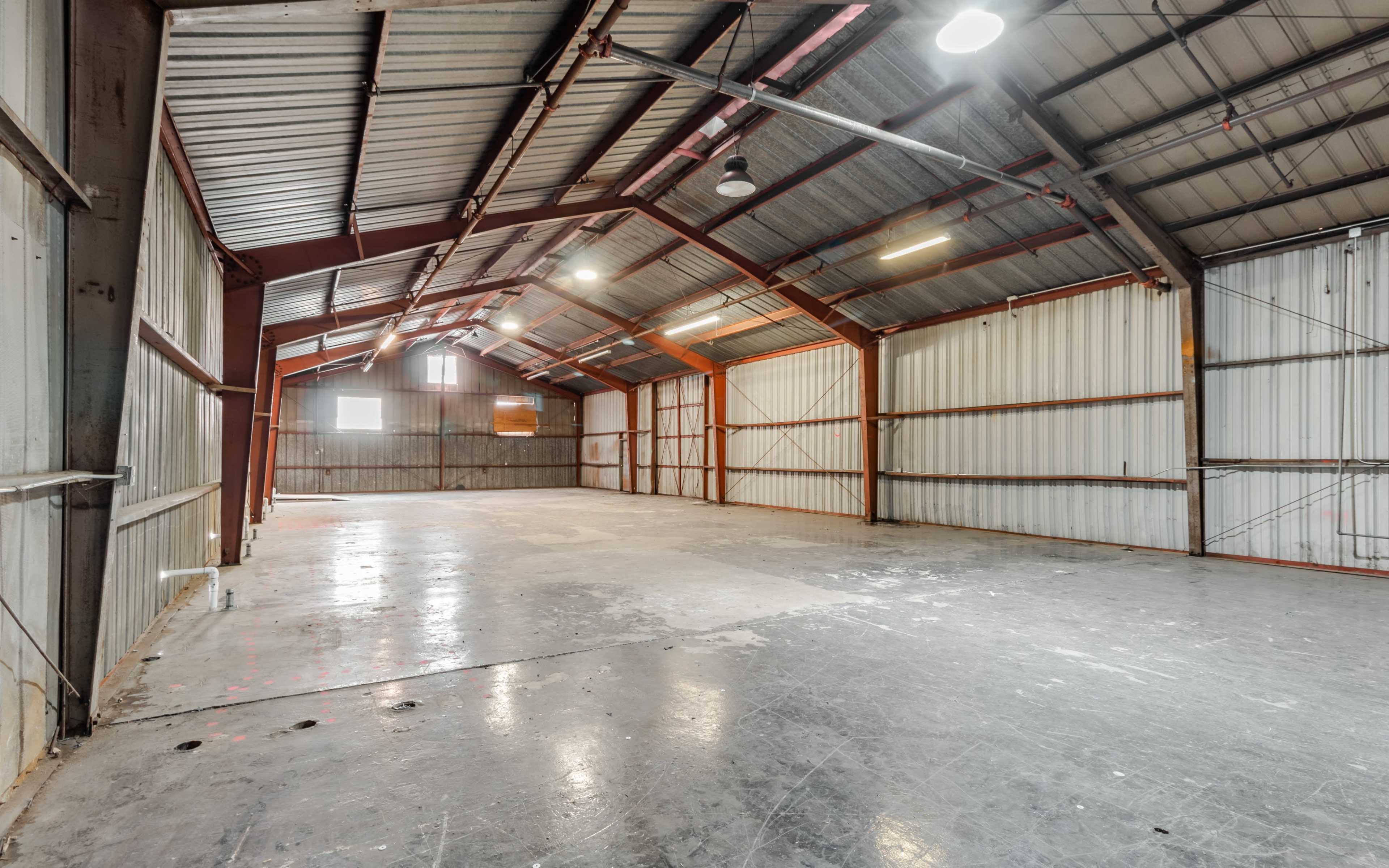 An empty industrial warehouse with metal beams, a high ceiling, and concrete flooring.