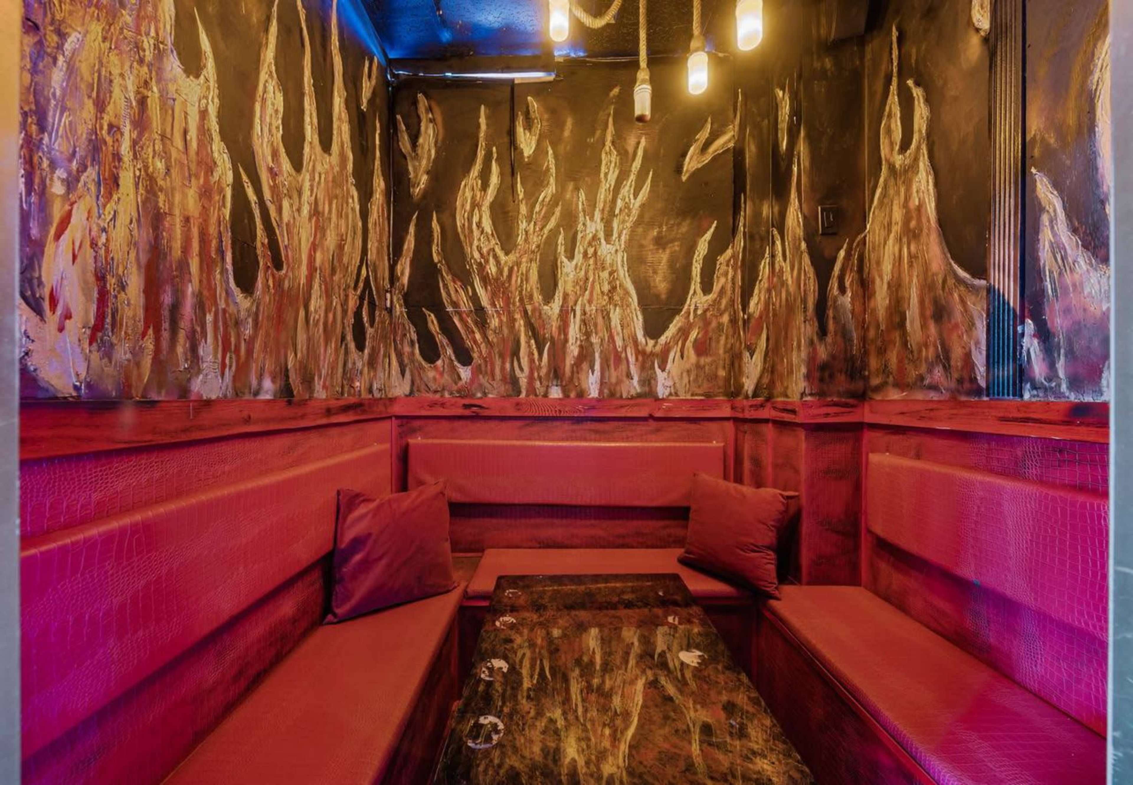 The image shows a cozy seating area with red upholstered benches, a dark marble table, and walls decorated with abstract flames.
