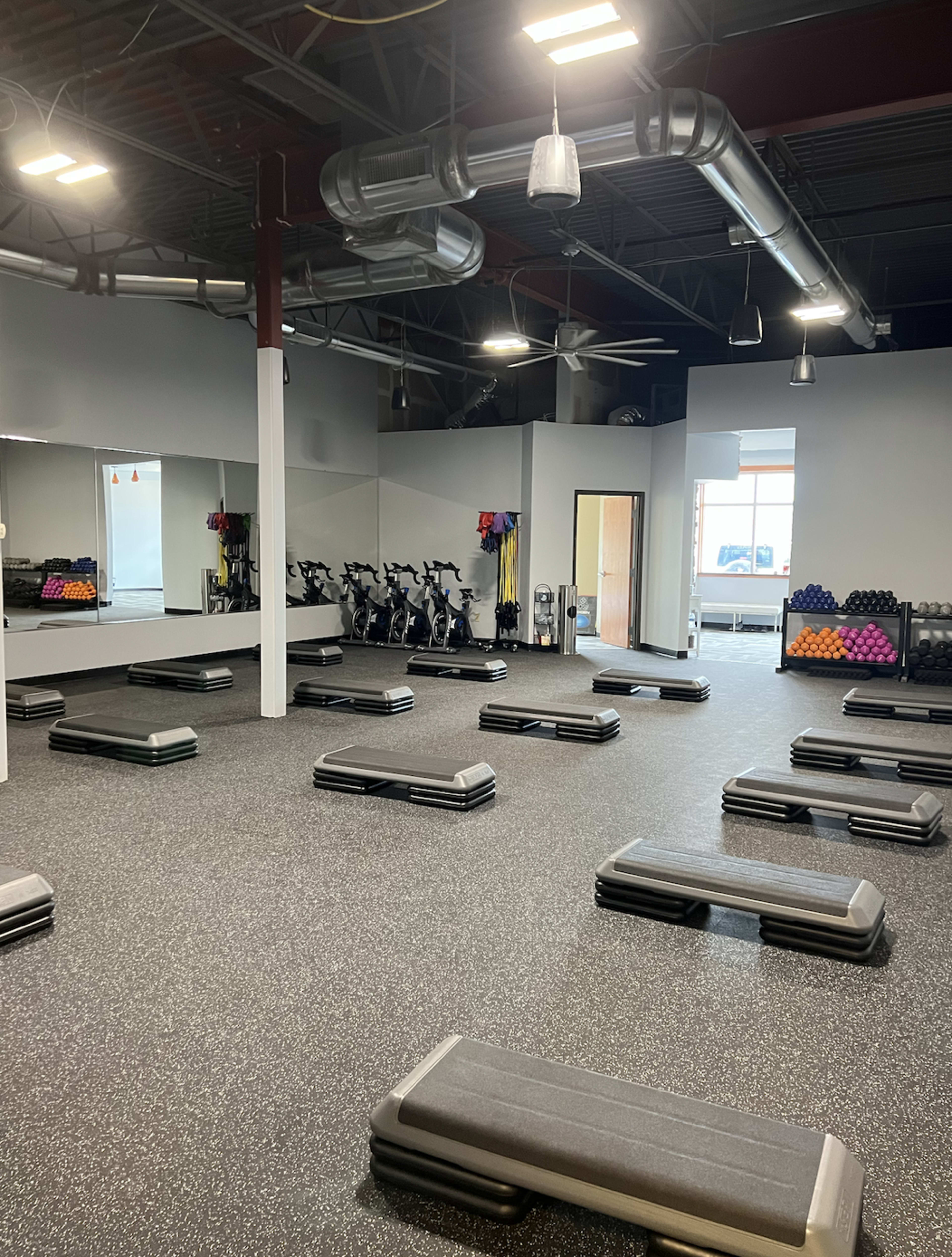An empty gym space featuring multiple workout benches arranged in rows, with exercise equipment and weights visible in the background.