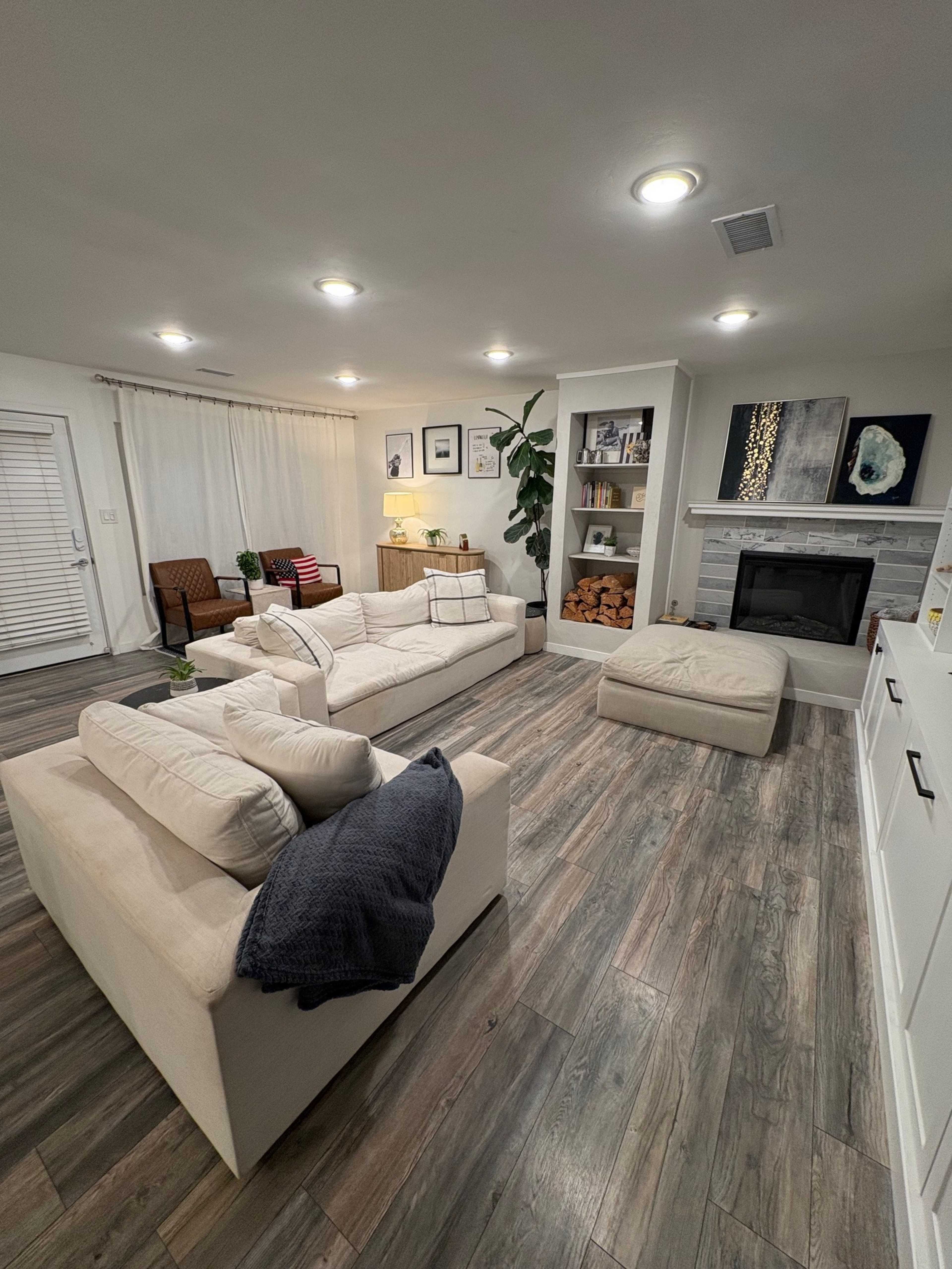 The living room features beige sofas, a decorative fireplace with stacked wood, and a combination of modern and minimalist decor.