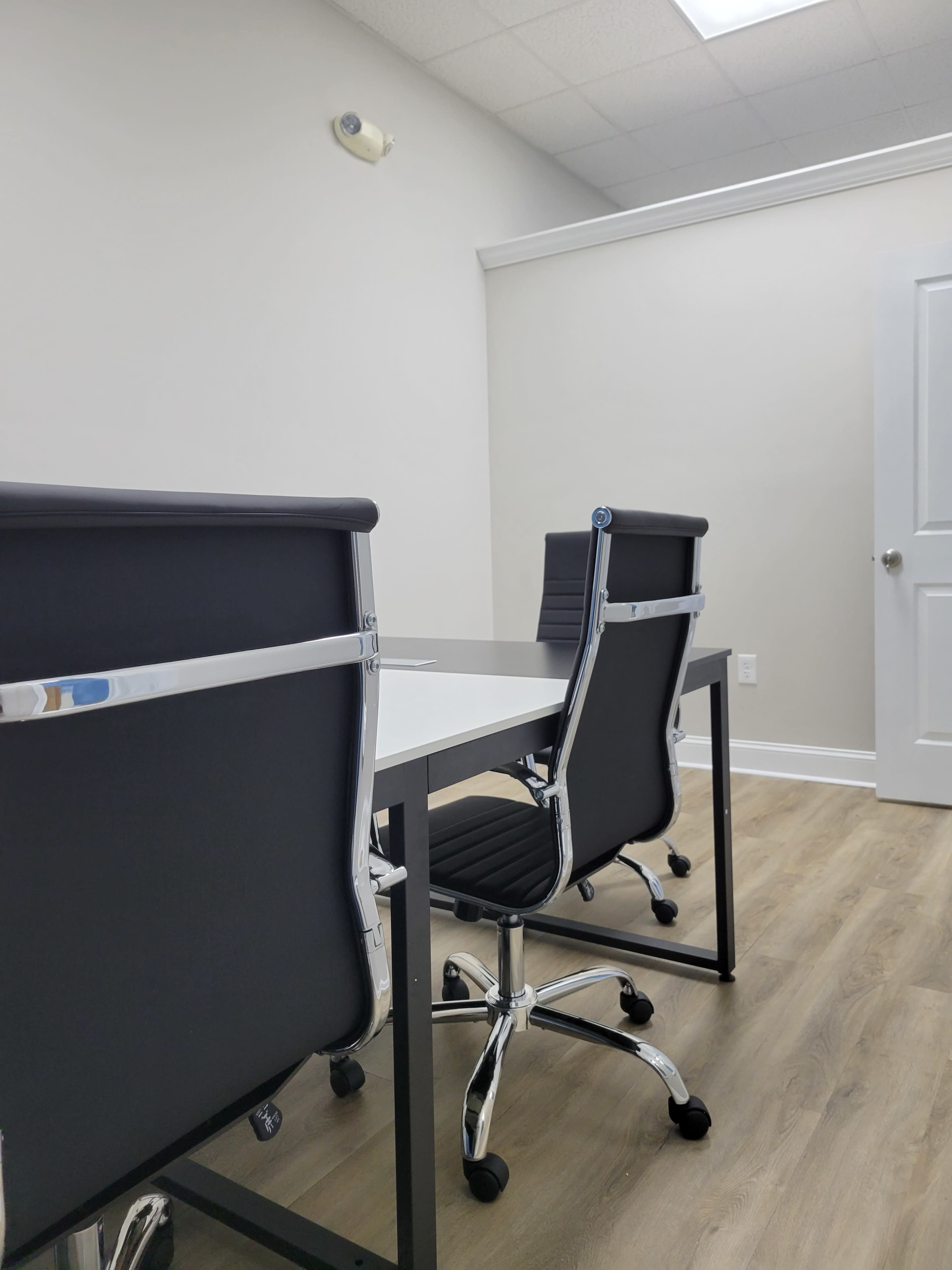 A modern office space with two black chairs positioned around a white desk, against a light-colored wall.
