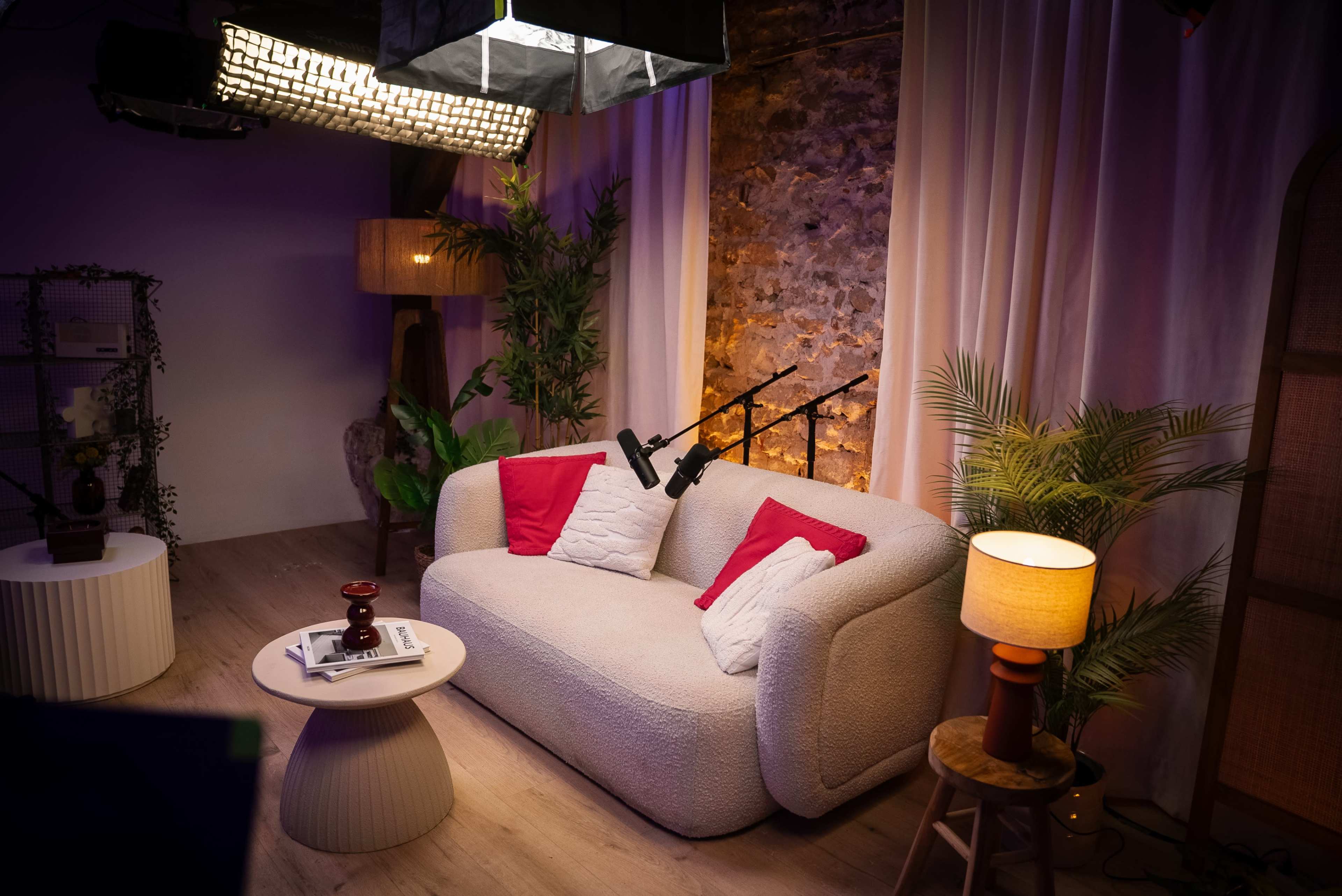 The image shows a cozy, modern living room setup with a light-colored sofa, a round coffee table, potted plants, and warm lighting.
