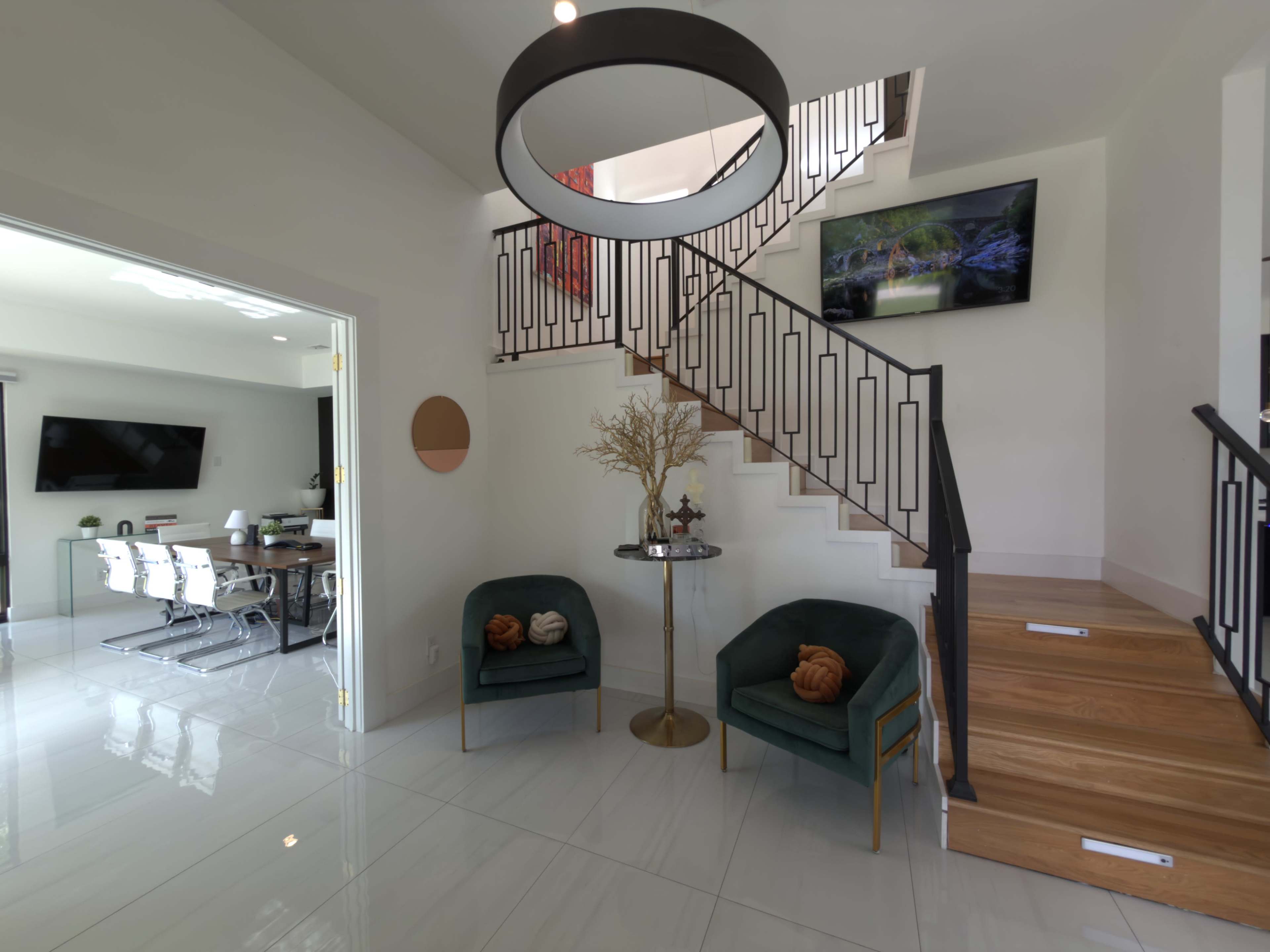 The image shows a modern foyer with a curved staircase, two green chairs with decorative pillows, and a dining area visible in the background.