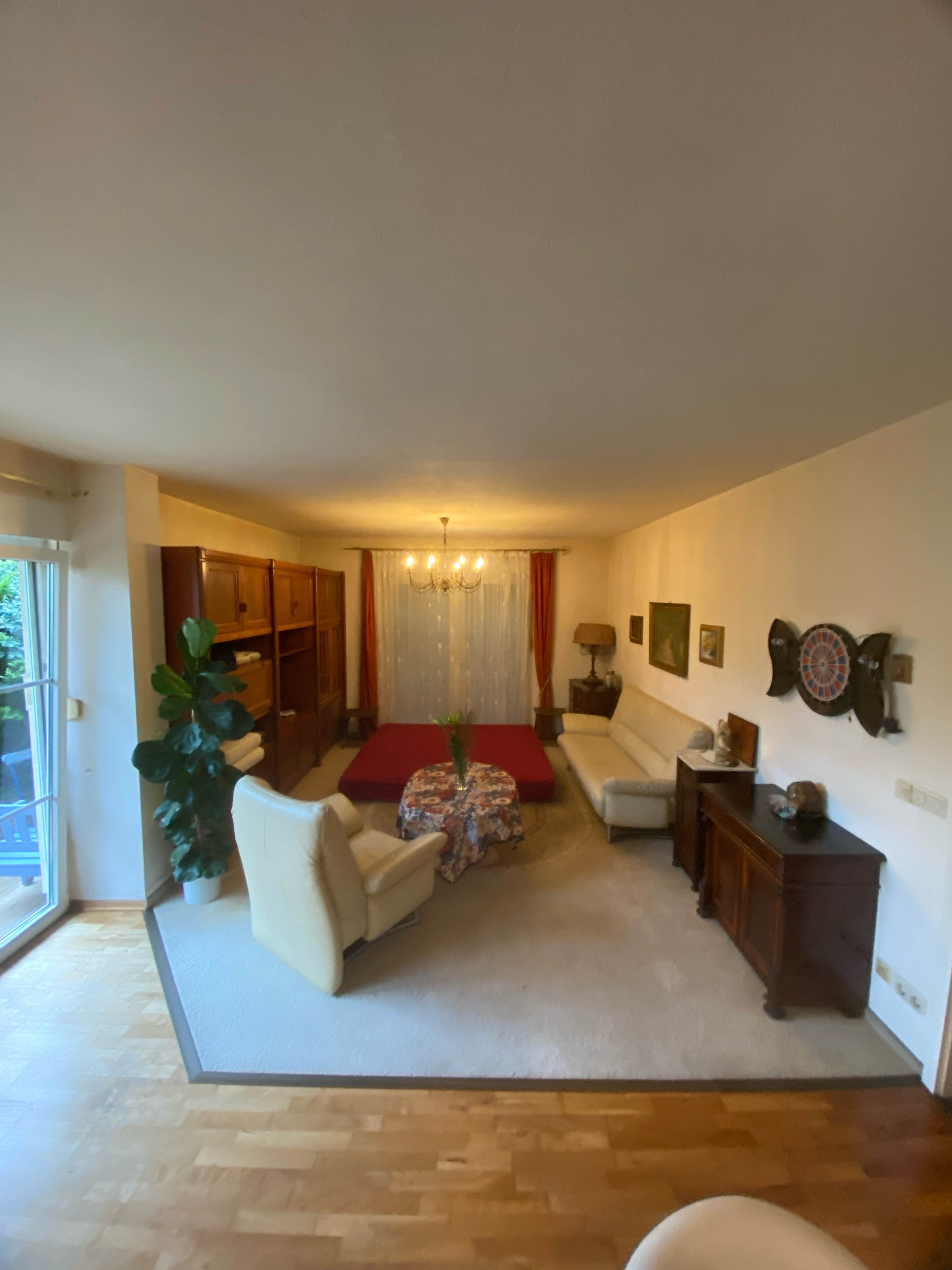 The image shows a living room furnished with two sofas, a coffee table with a floral tablecloth, and wooden cabinets, illuminated by a chandelier.