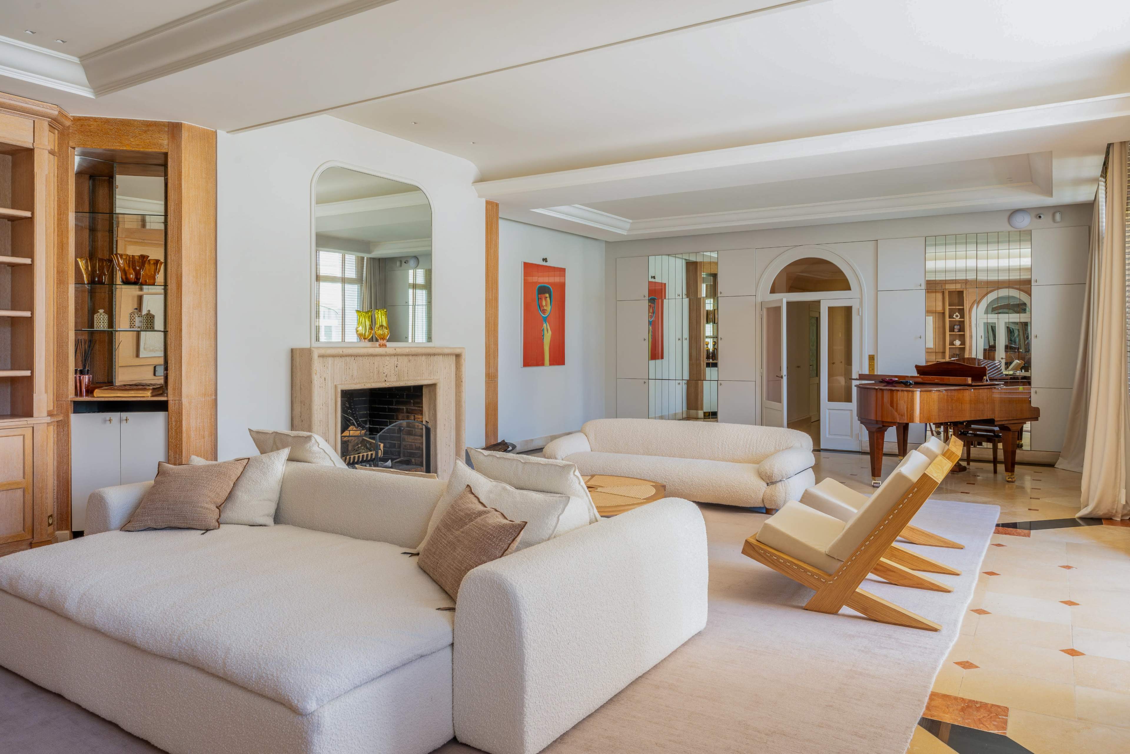 The image shows a spacious living area featuring a light-colored sofa, a wooden grand piano, and a fireplace, with artwork and decorative elements on the walls.