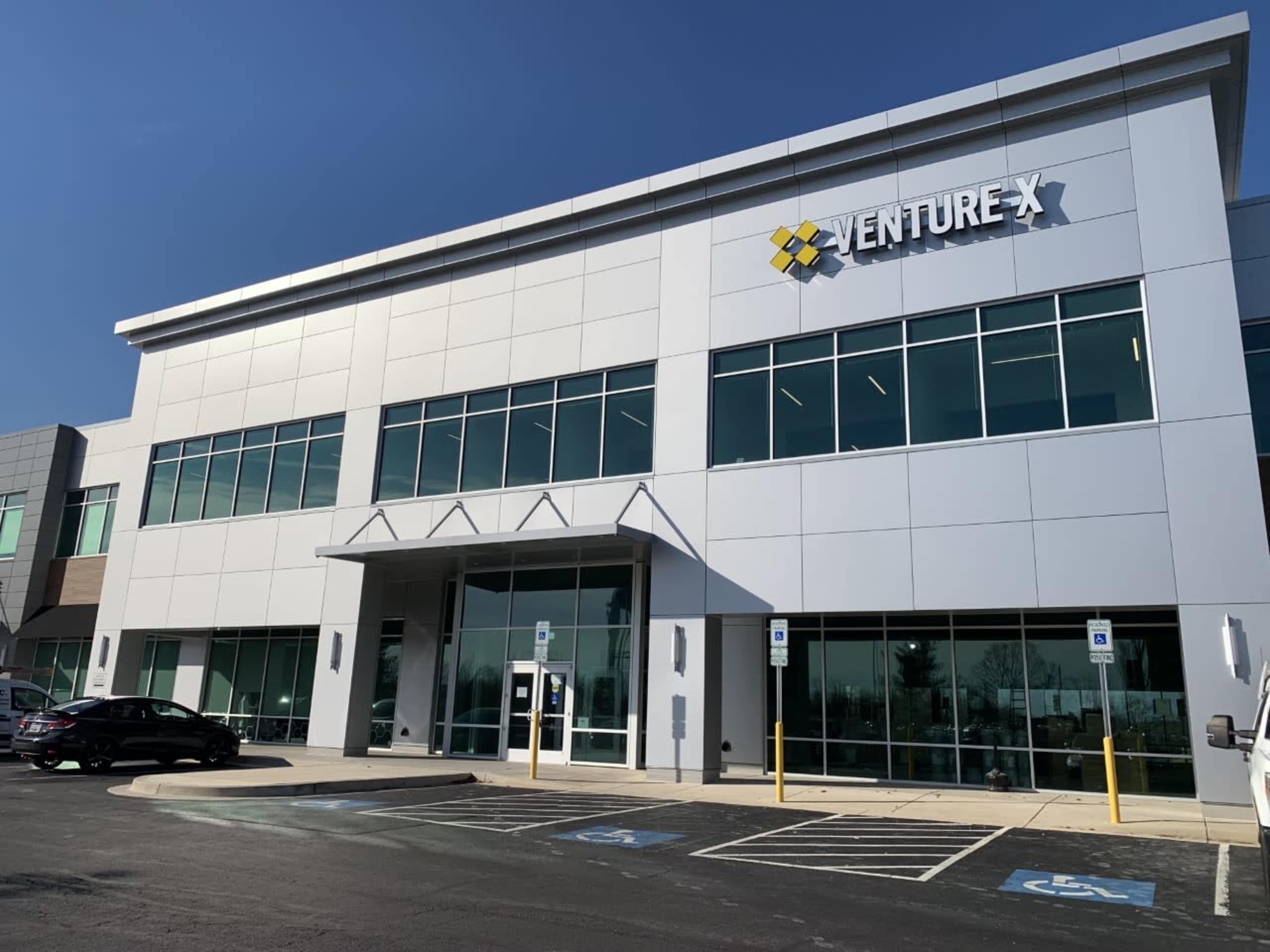 The image shows a modern, two-story office building with large glass windows and the sign "VENTURE X" displayed prominently on the facade.