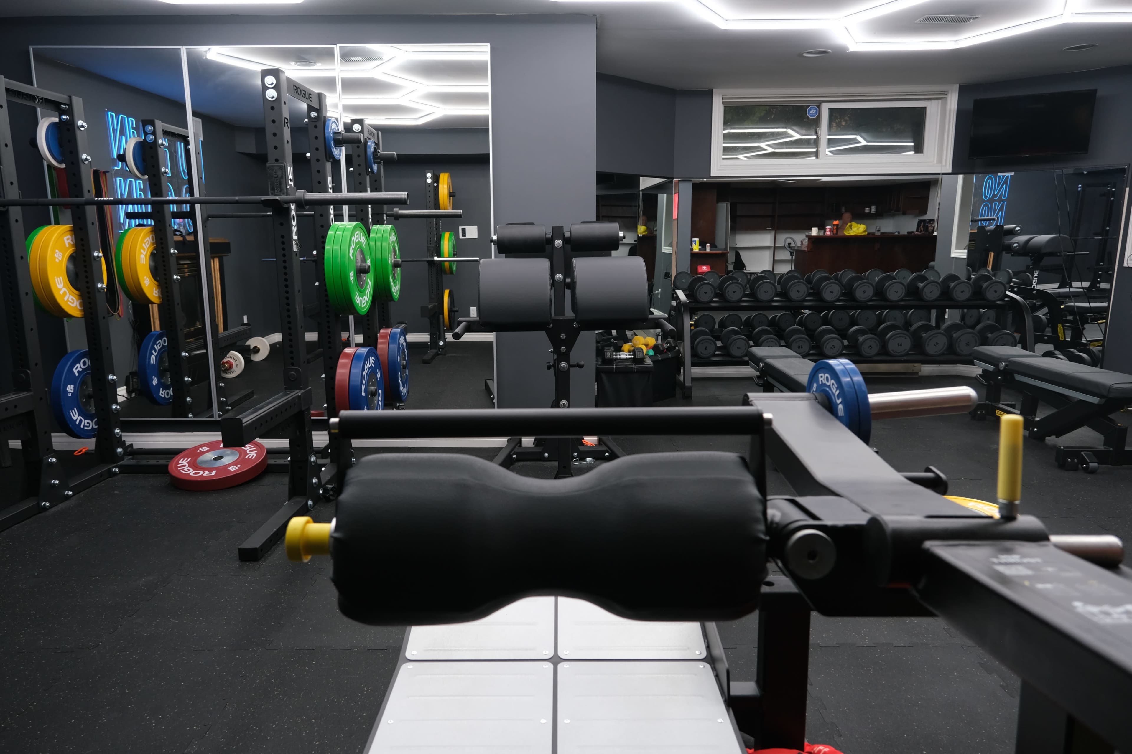 A well-equipped modern gym with various weightlifting equipment, including barbells, dumbbells, and benches, arranged in a spacious setting.