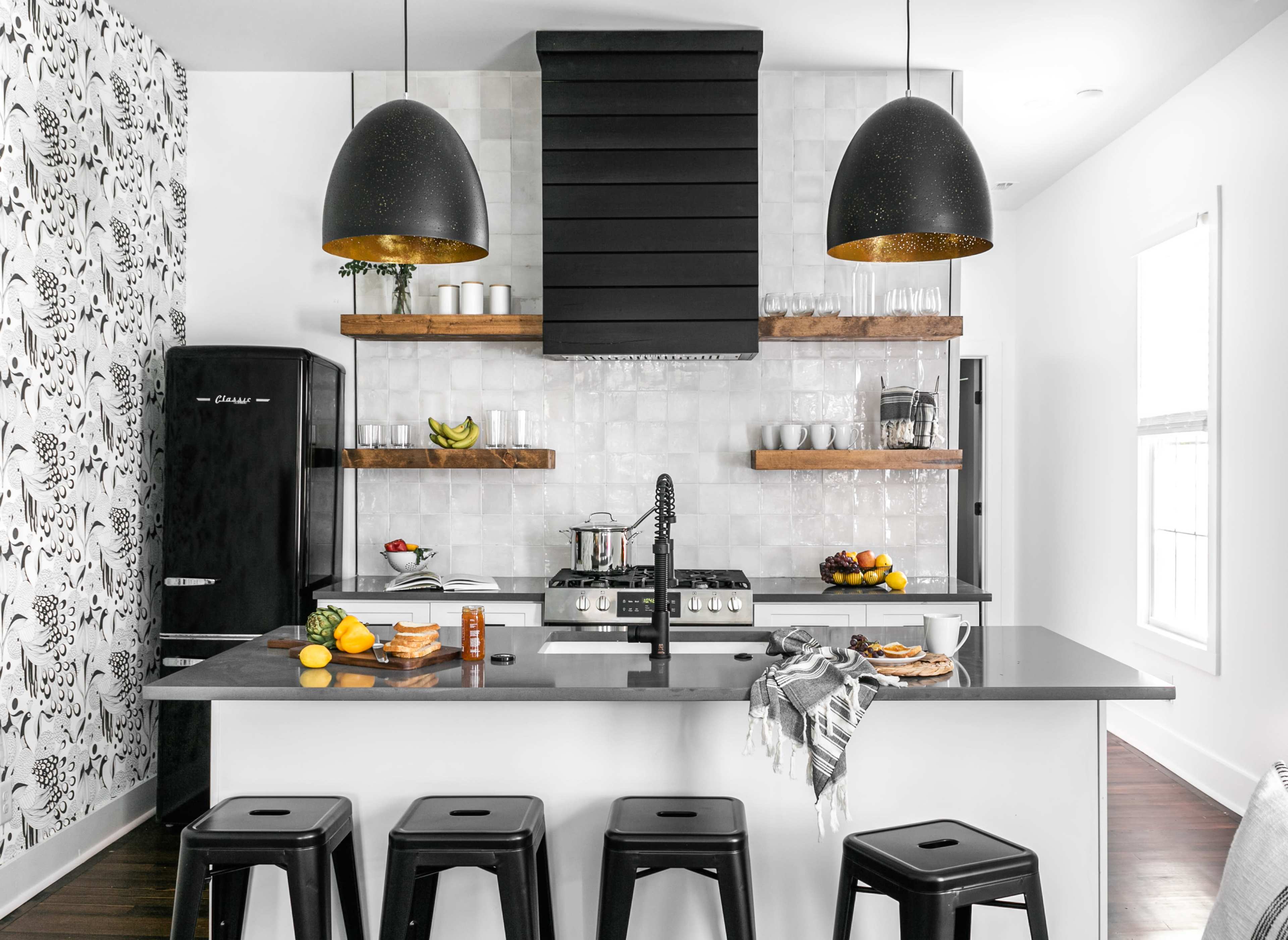 A modern kitchen with black cabinetry, a central island with bar stools, and open shelving displaying kitchenware and fruits.