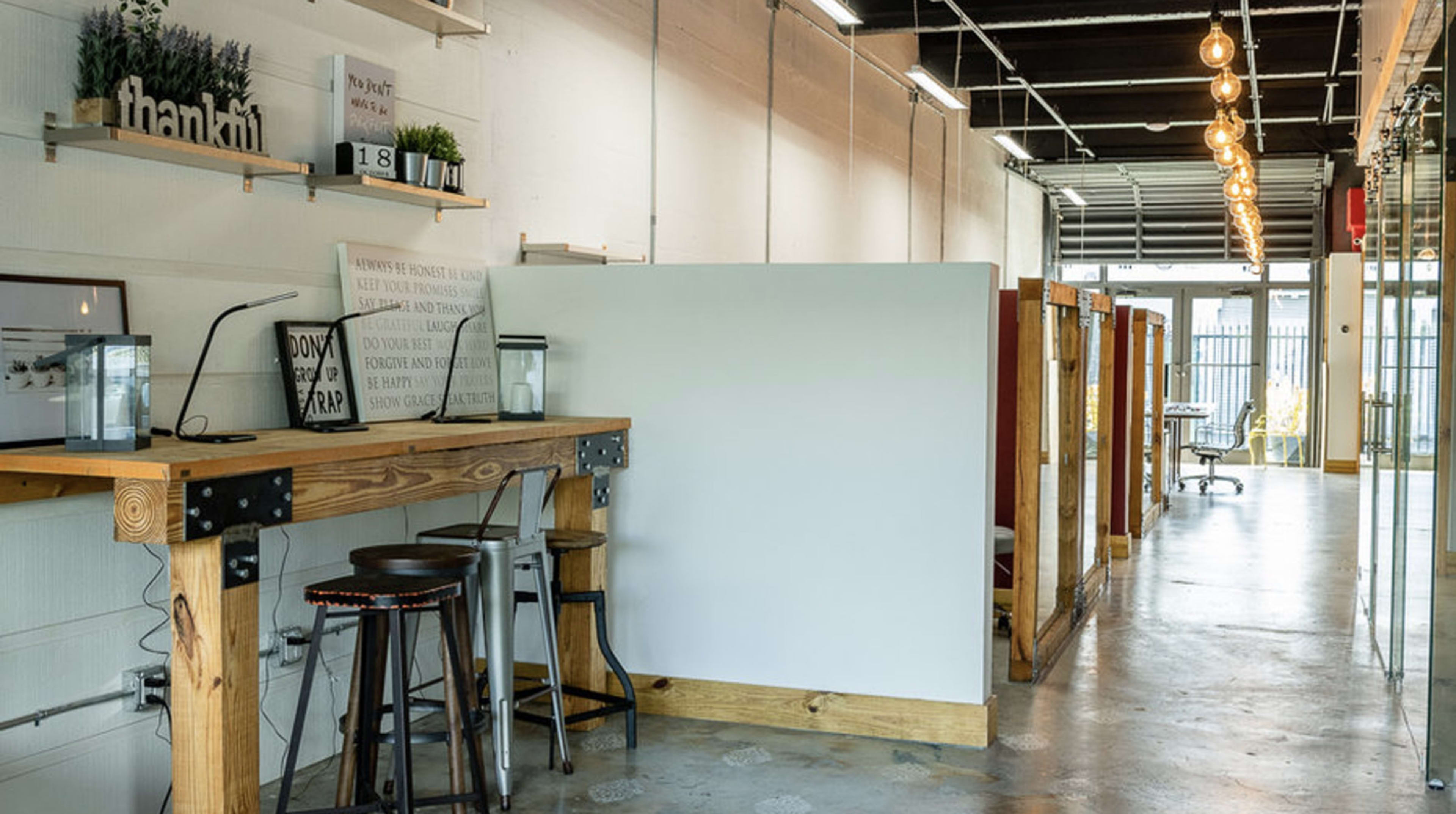 A modern co-working space with wooden workstations, partitioned areas, and overhead lighting along a long corridor.