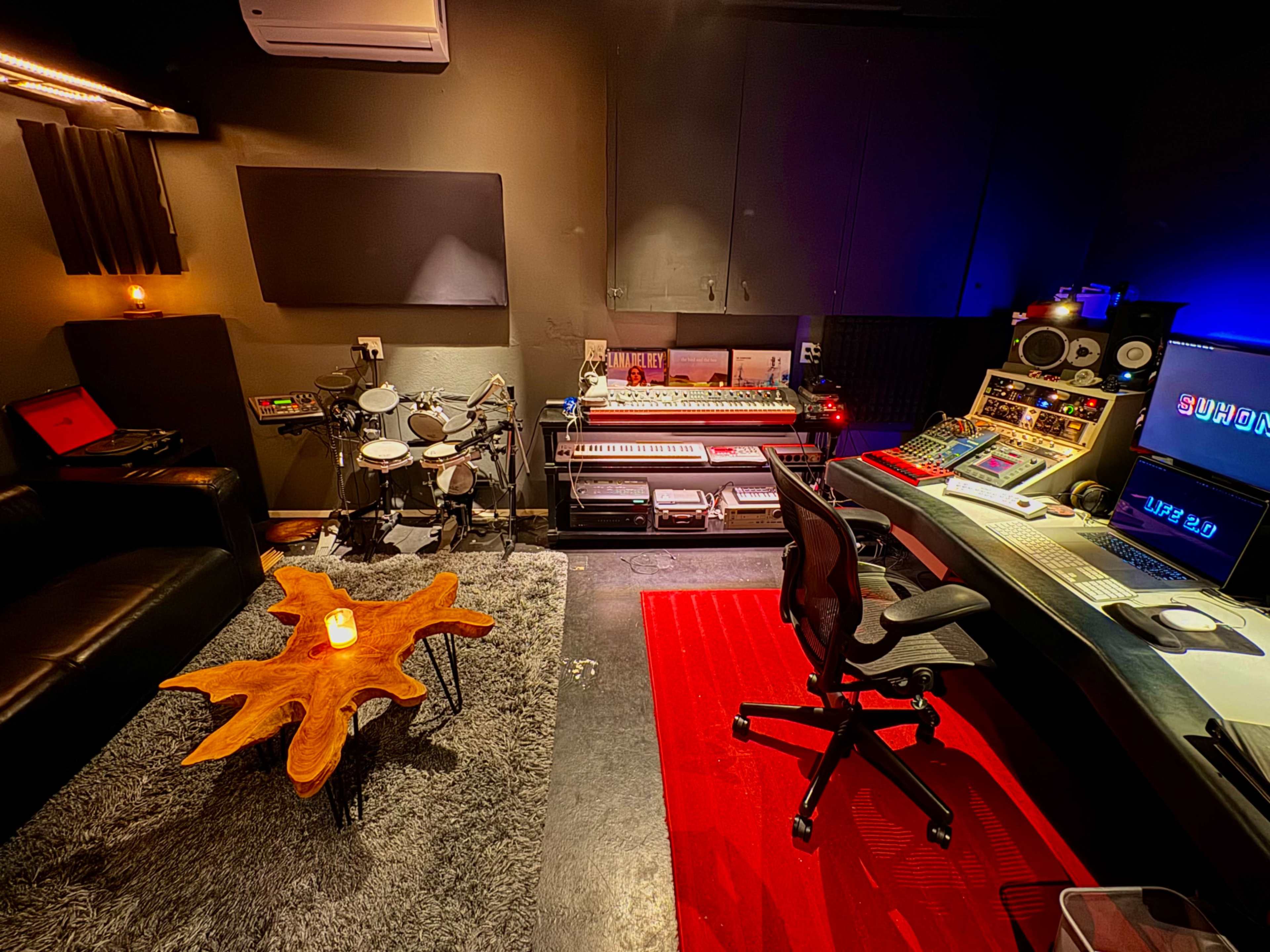 A music production studio featuring a mix of electronic equipment, a cozy seating area, and a drum set.