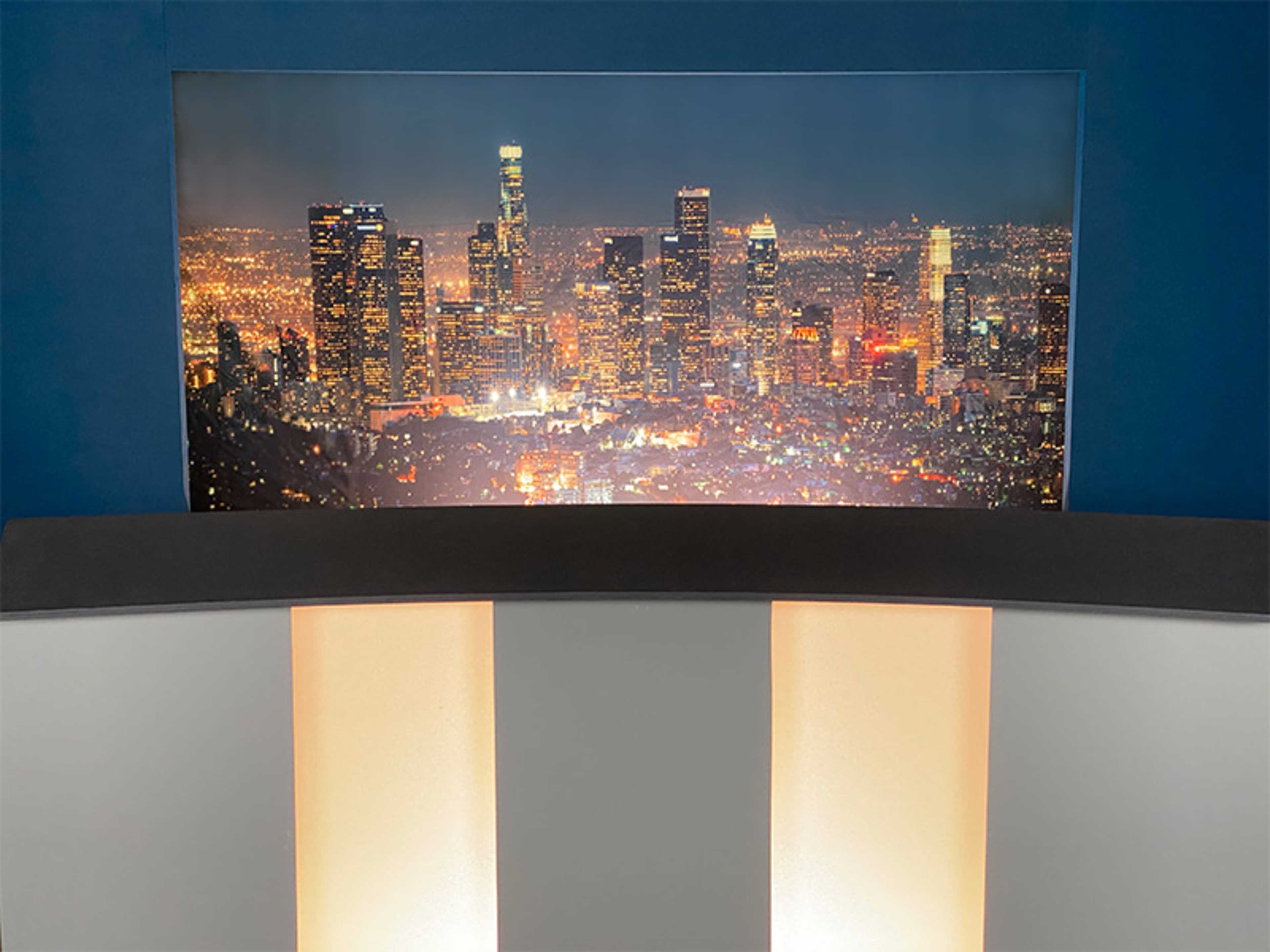 A city skyline of Los Angeles illuminated at night, with a dark background and a curved desk in the foreground.