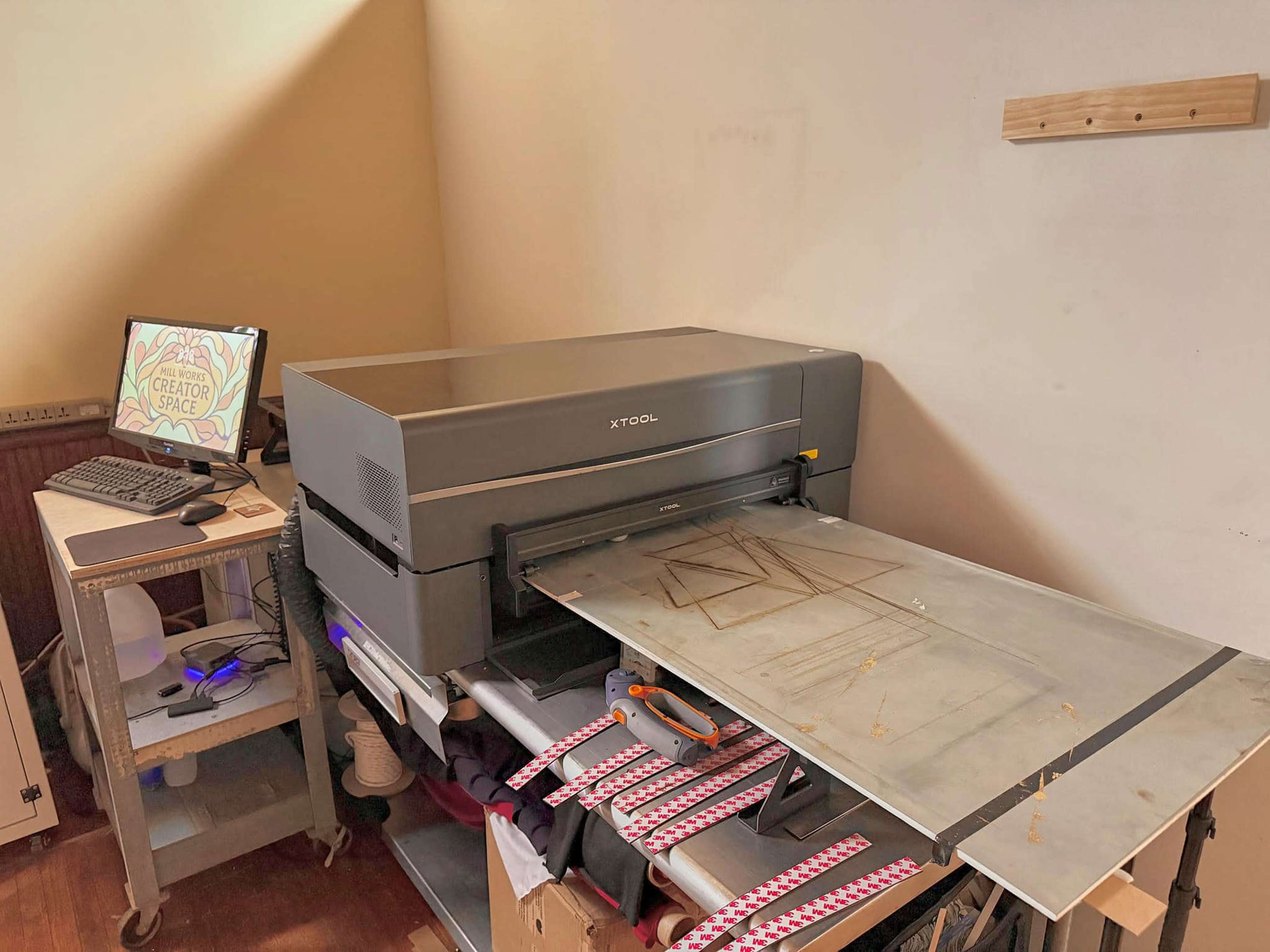 A large printer is set up on a table next to a computer in a workspace.
