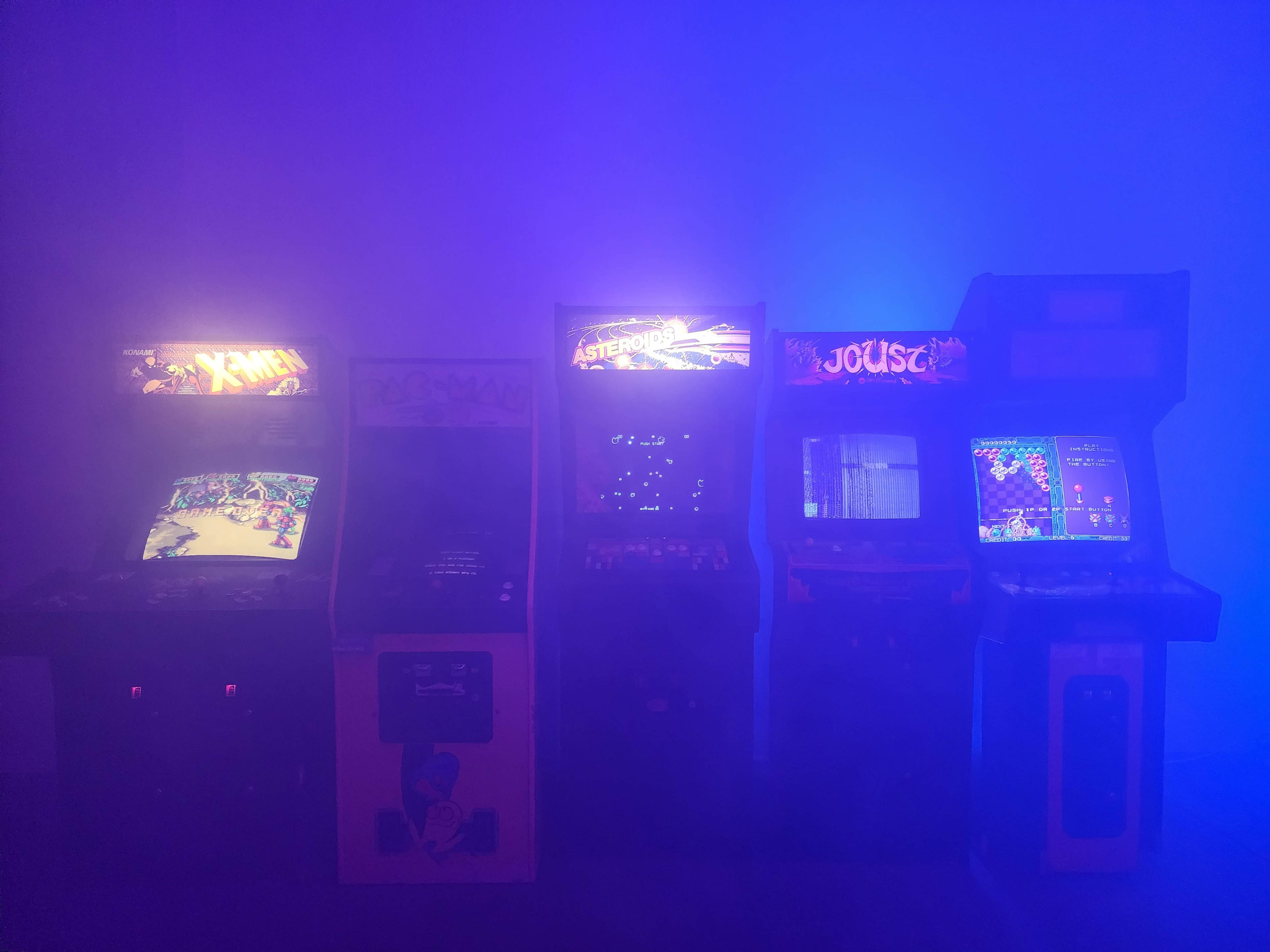 A row of classic arcade game machines illuminated by a blue haze.