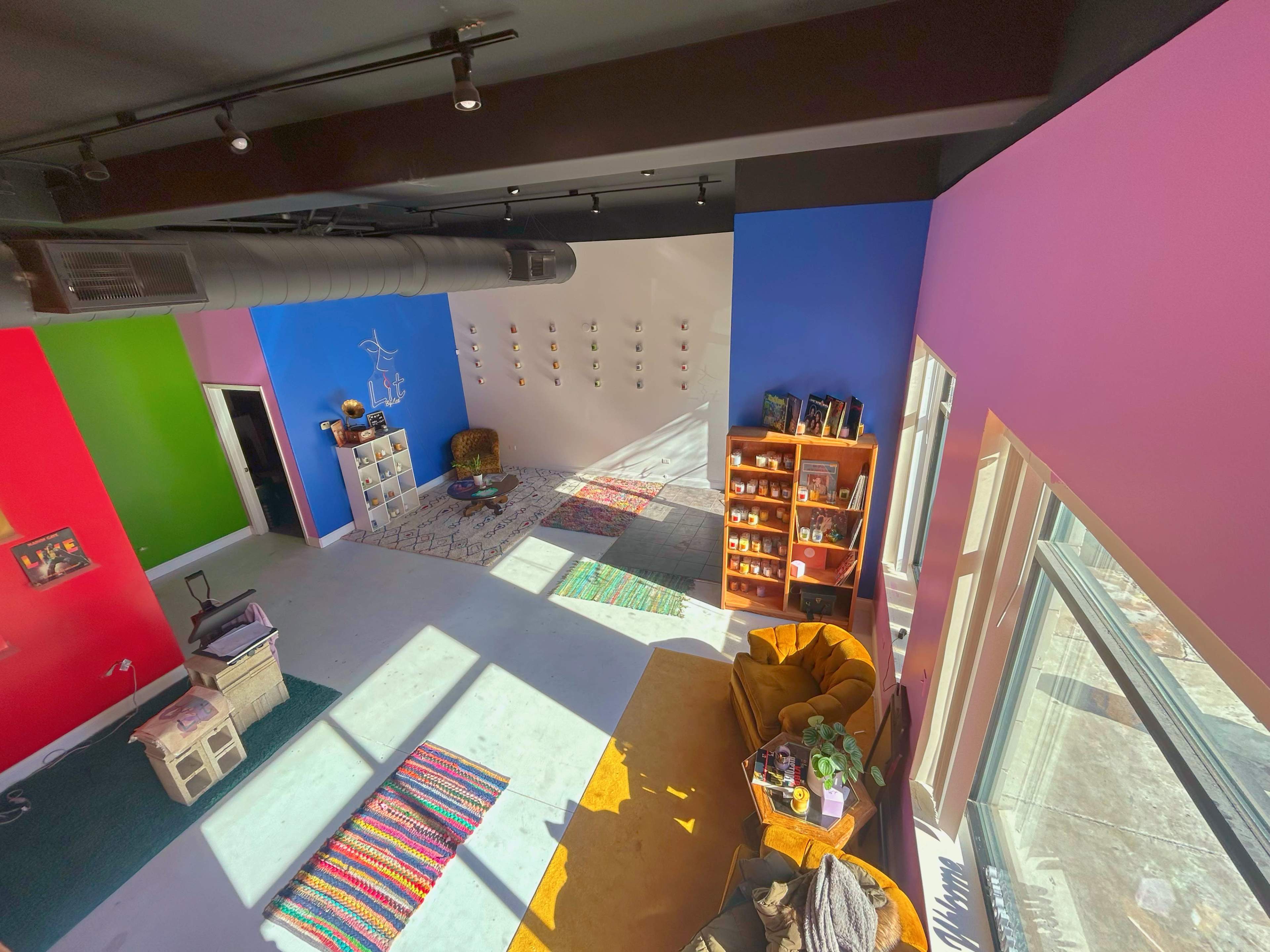 A brightly colored room with various seating areas, shelves filled with items, and a large window allowing natural light to enter.