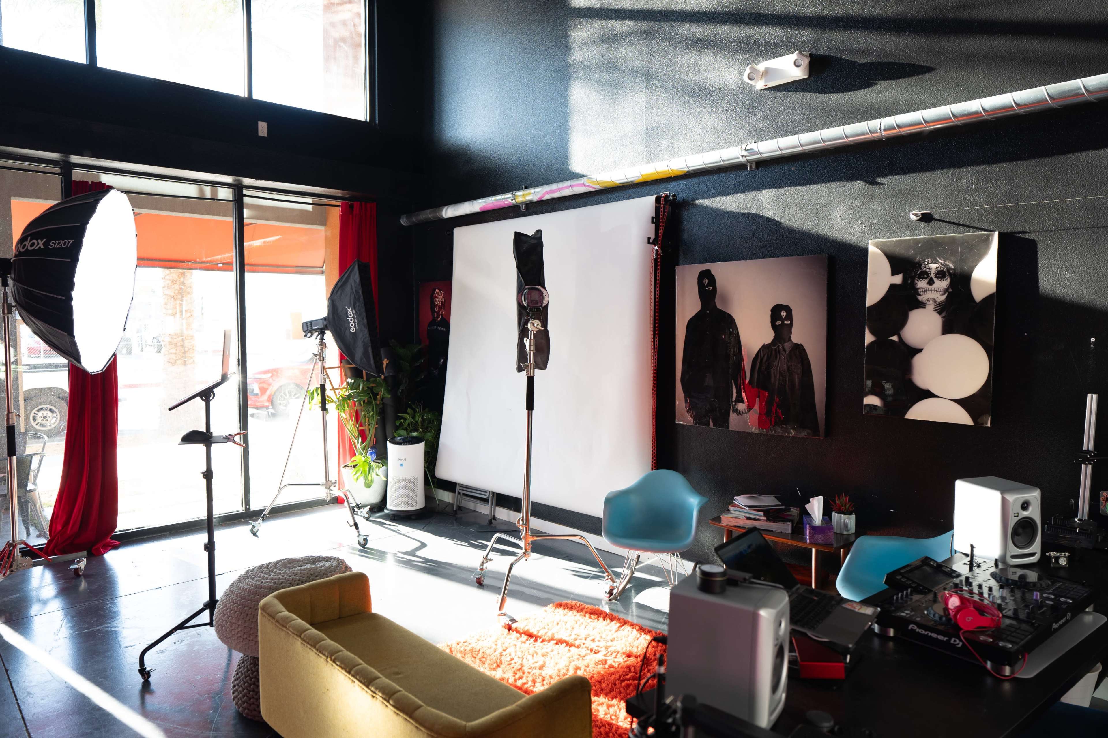 A photography studio features a large backdrop, studio equipment, and vibrant decor, with sunlight casting shadows on the walls and furniture.