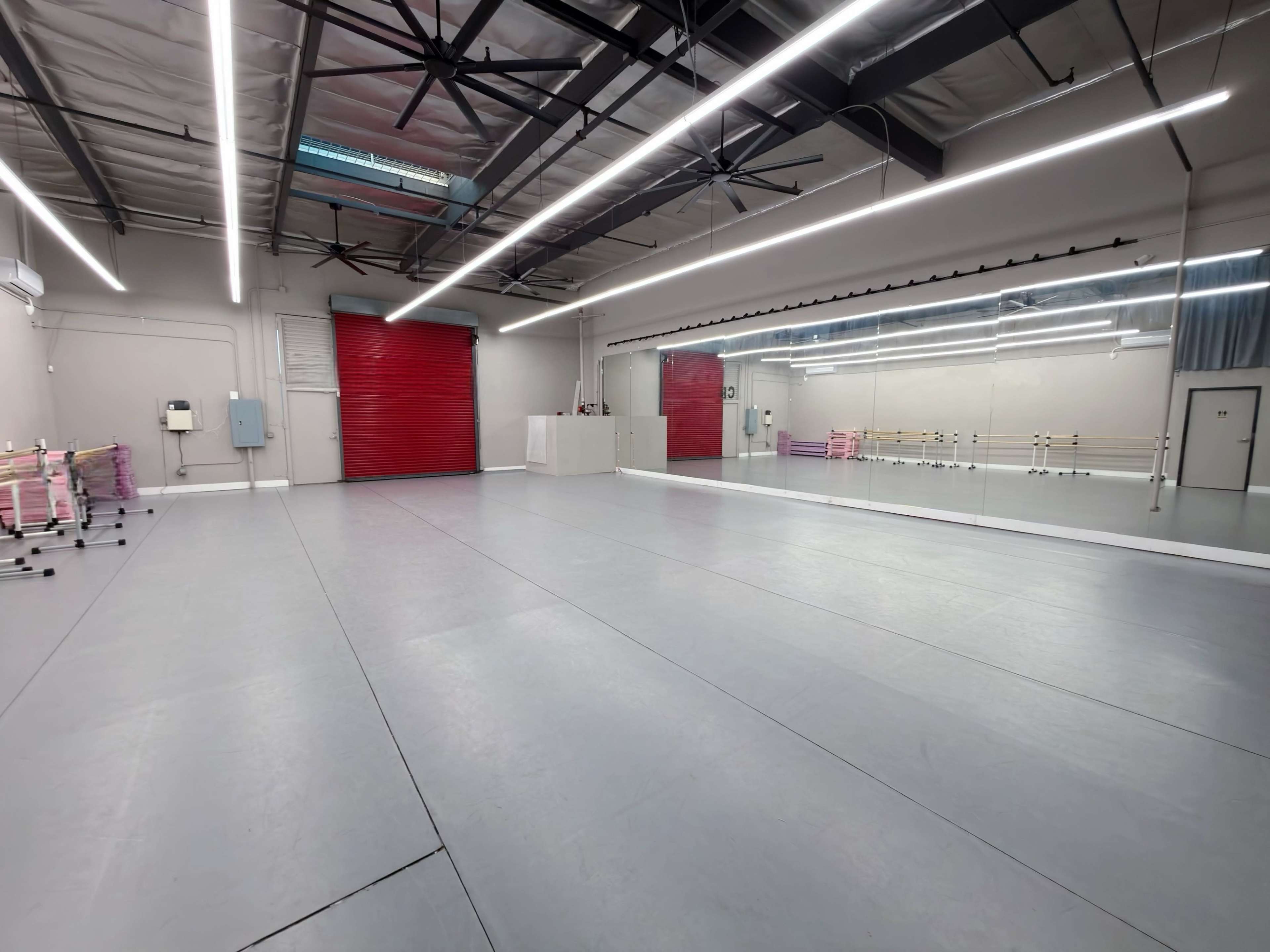 The image shows a spacious dance studio with a large mirror on one wall, a red sliding door, and light gray flooring.