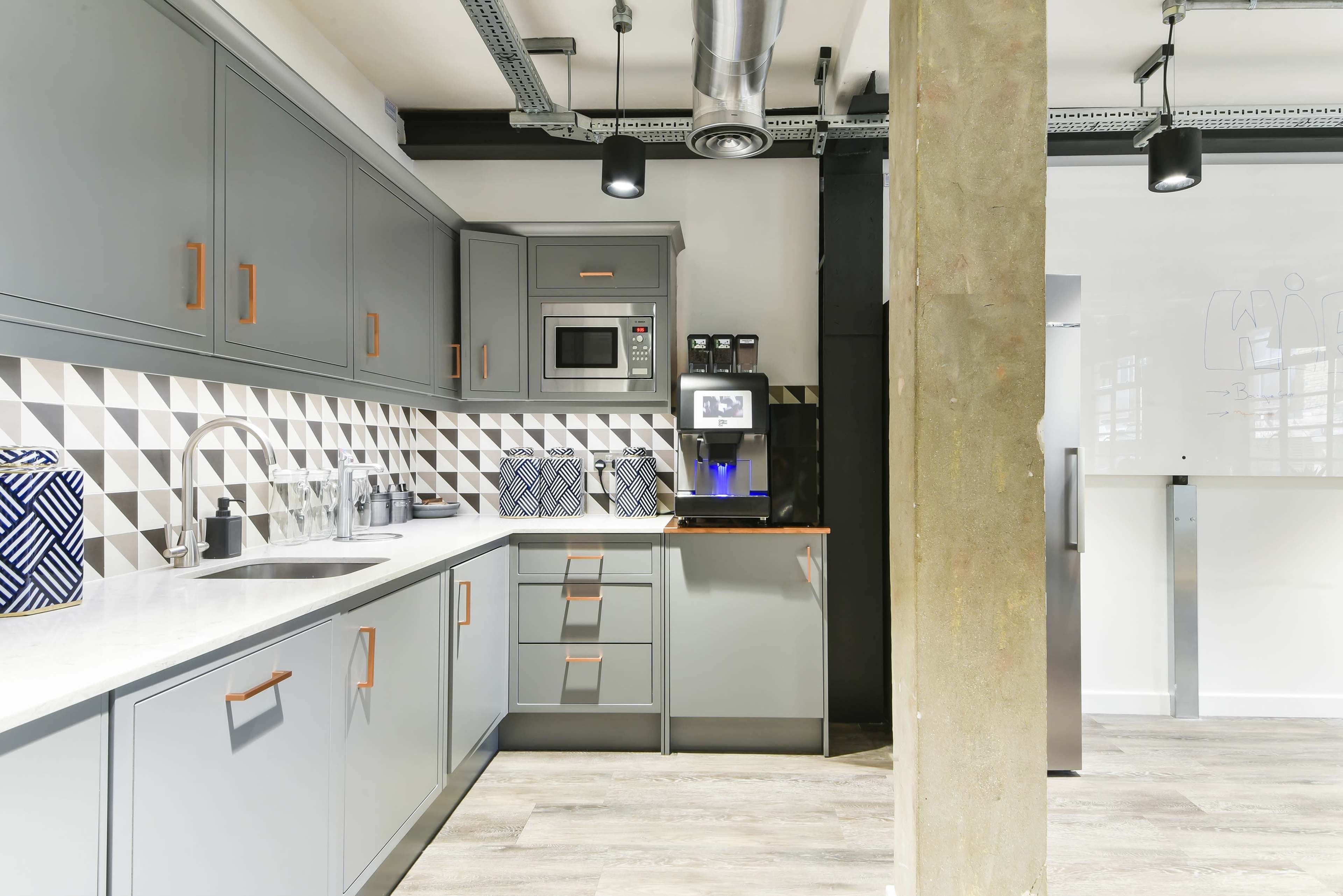 A modern kitchen with gray cabinetry, a patterned backsplash, and stainless steel appliances.