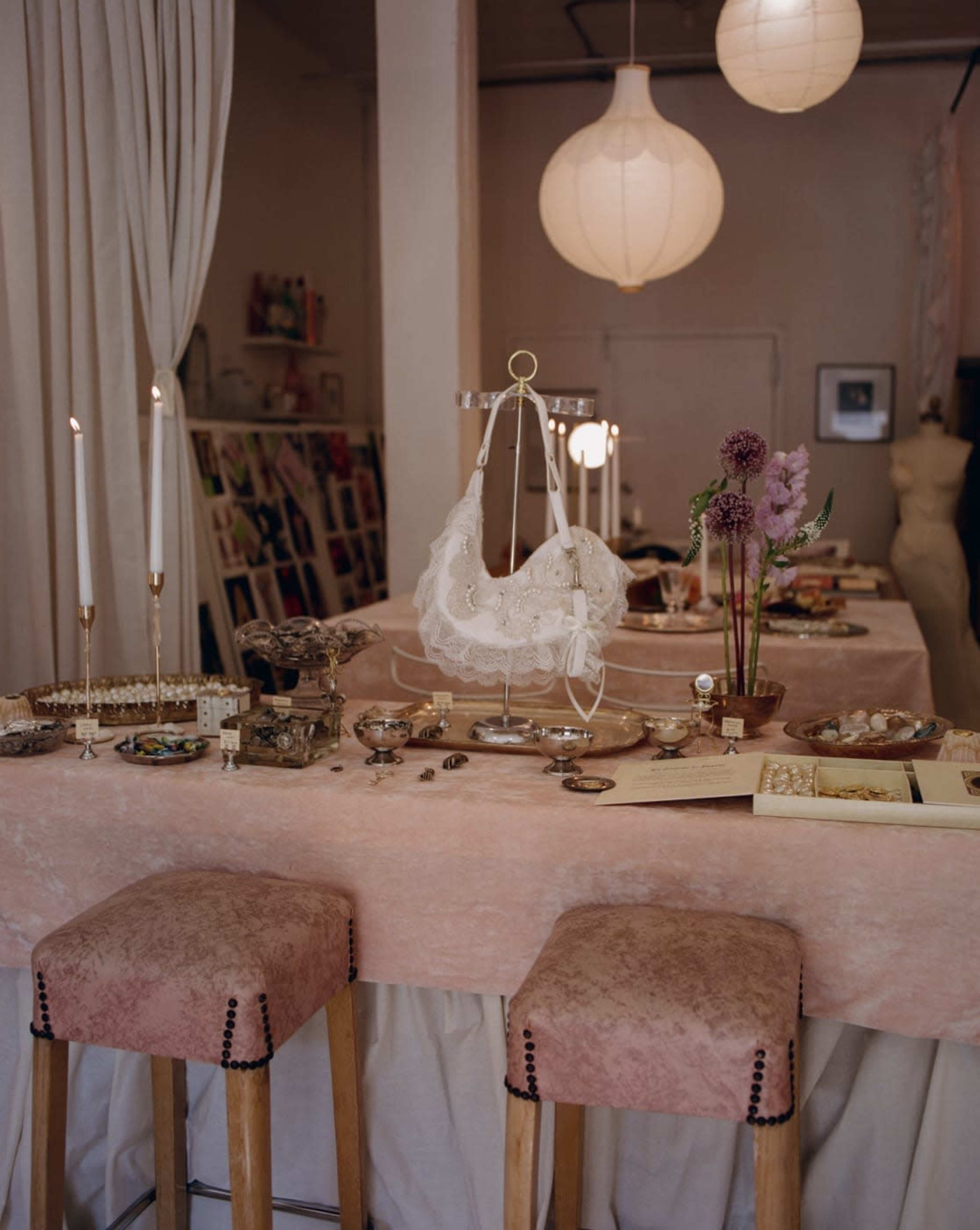 The image shows a well-decorated table featuring various jewelry items, candles, flowers, and elegant decor in a softly lit space.