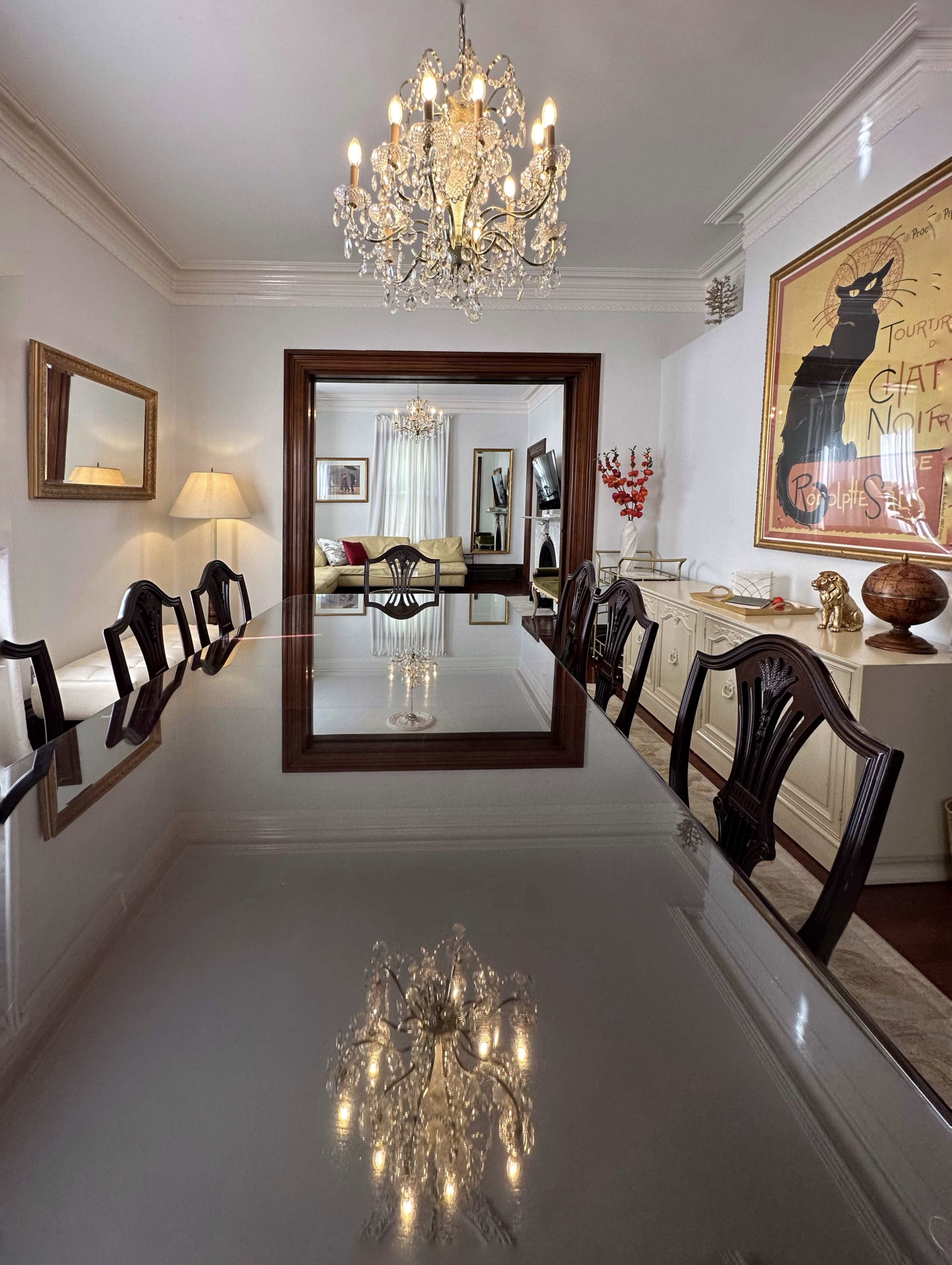 A long dining table reflects a chandelier and a large mirror in a well-decorated dining room.