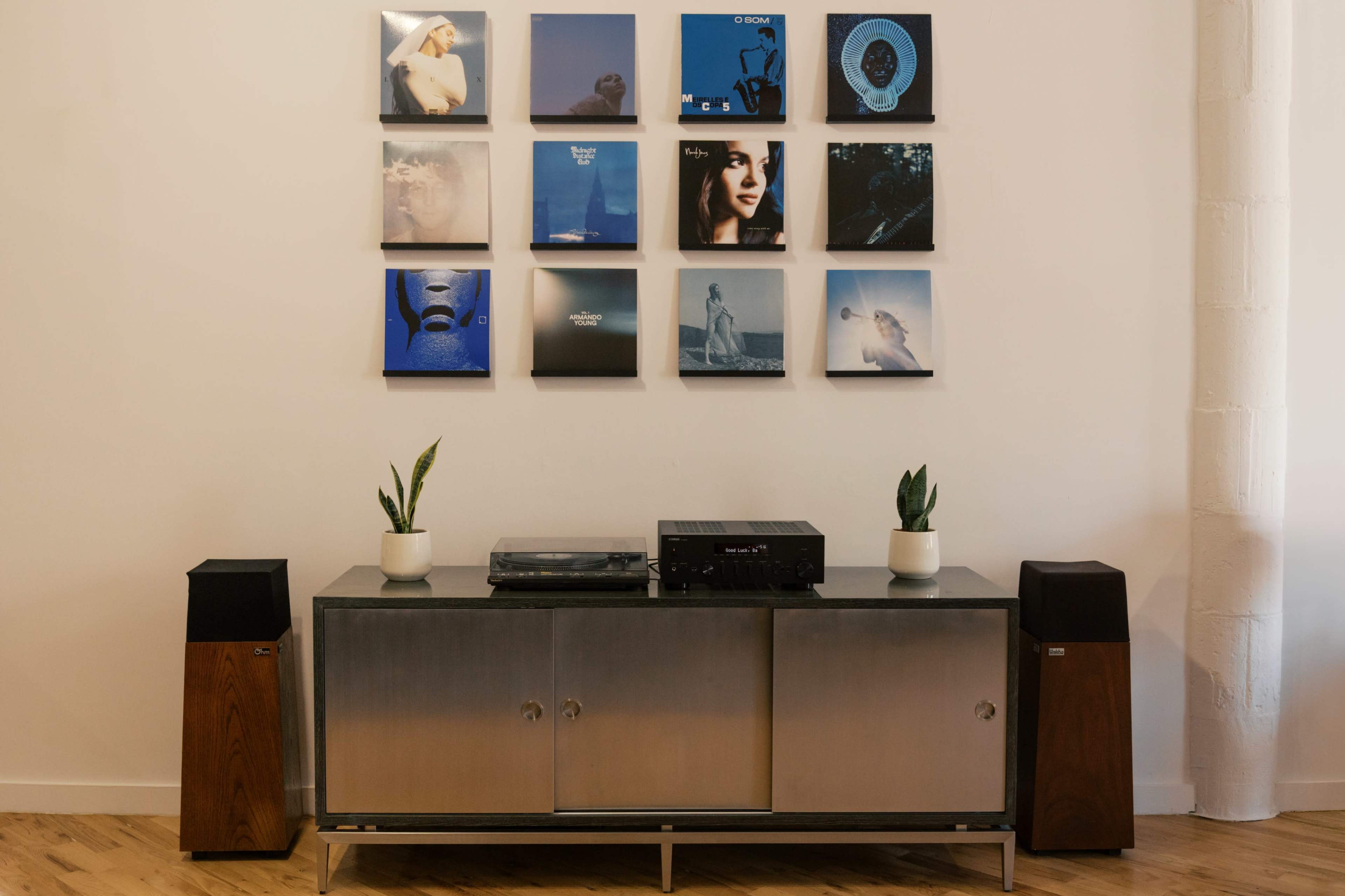 A wooden cabinet with a turntable and speakers sits against a wall adorned with framed album covers.
