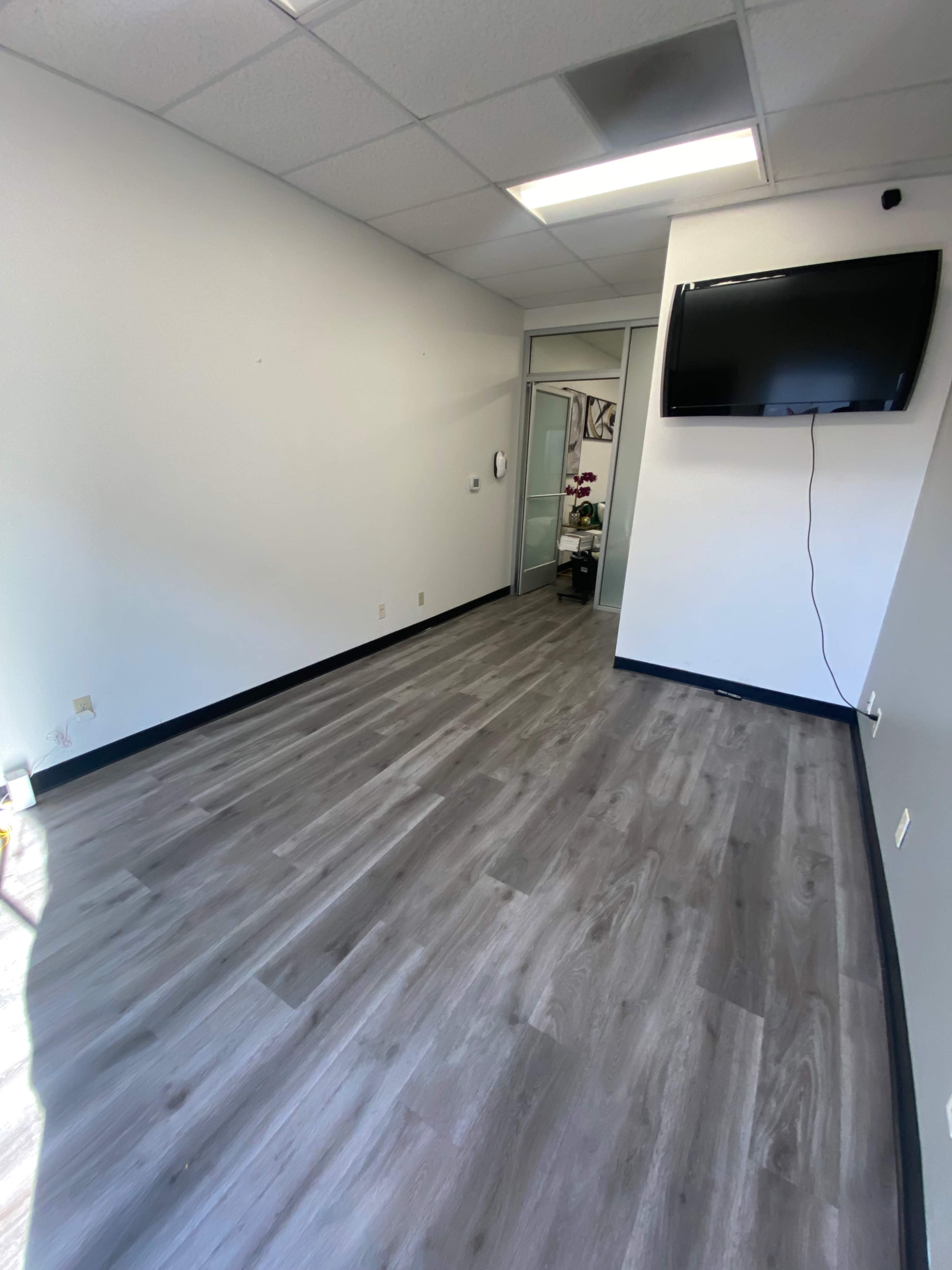 An empty office space with gray flooring and a wall-mounted television.